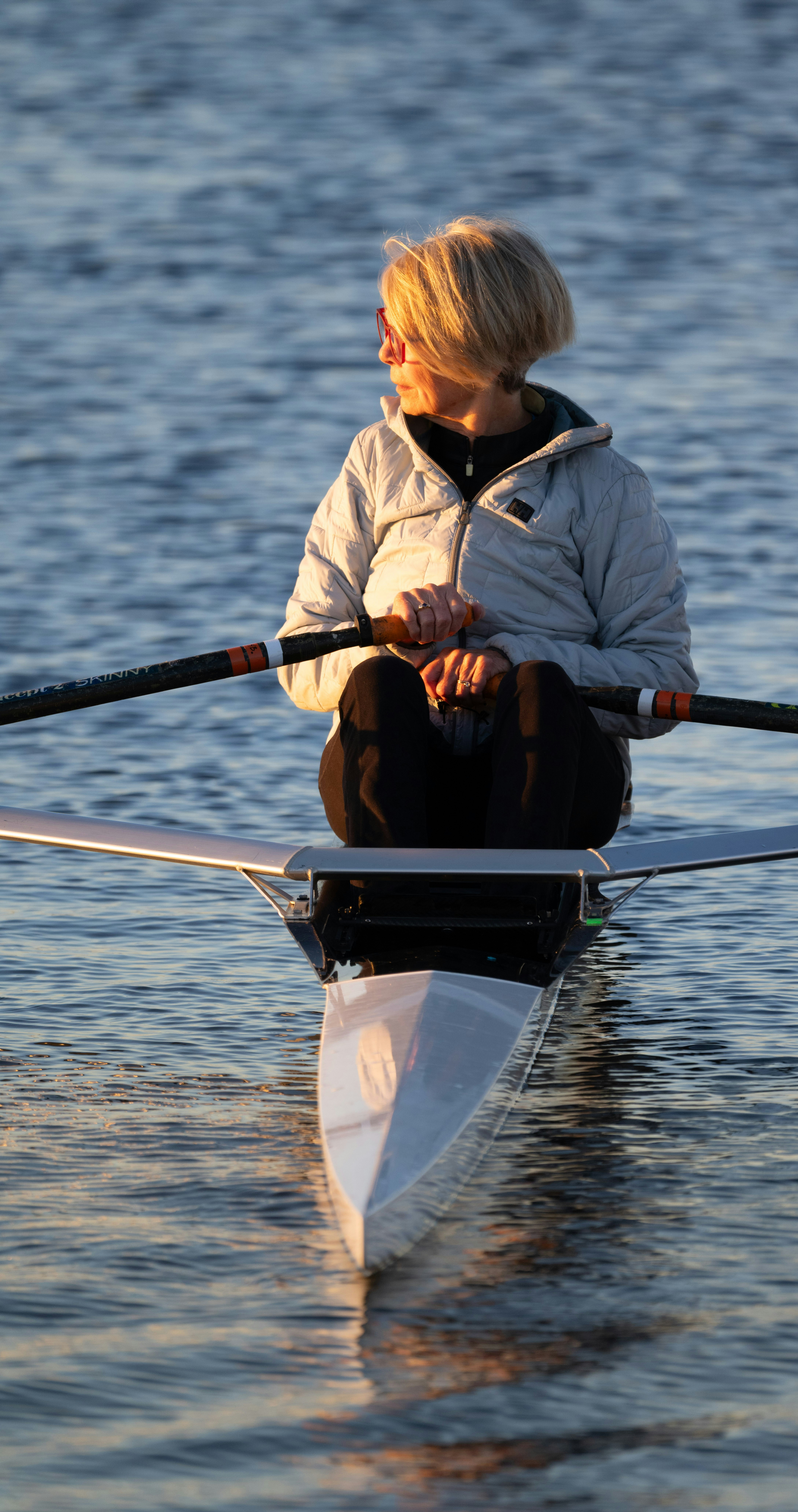 Woman rows a boat on a calm body of water.