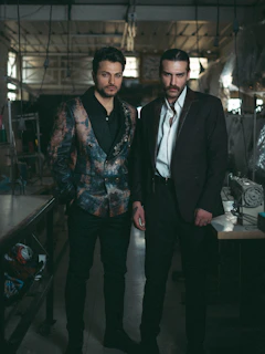 Two men pose inside a workshop.