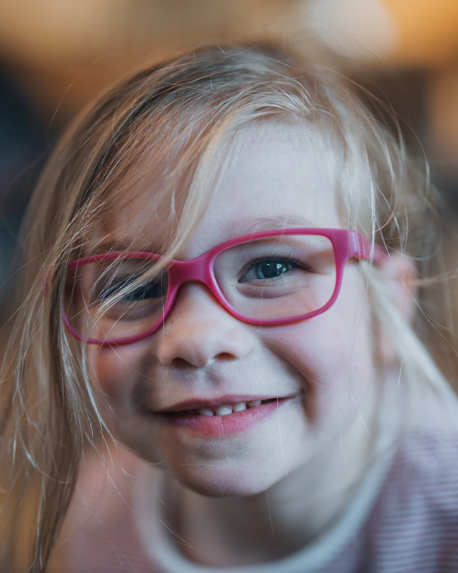 A cute little girl is smiling, wearing glasses.