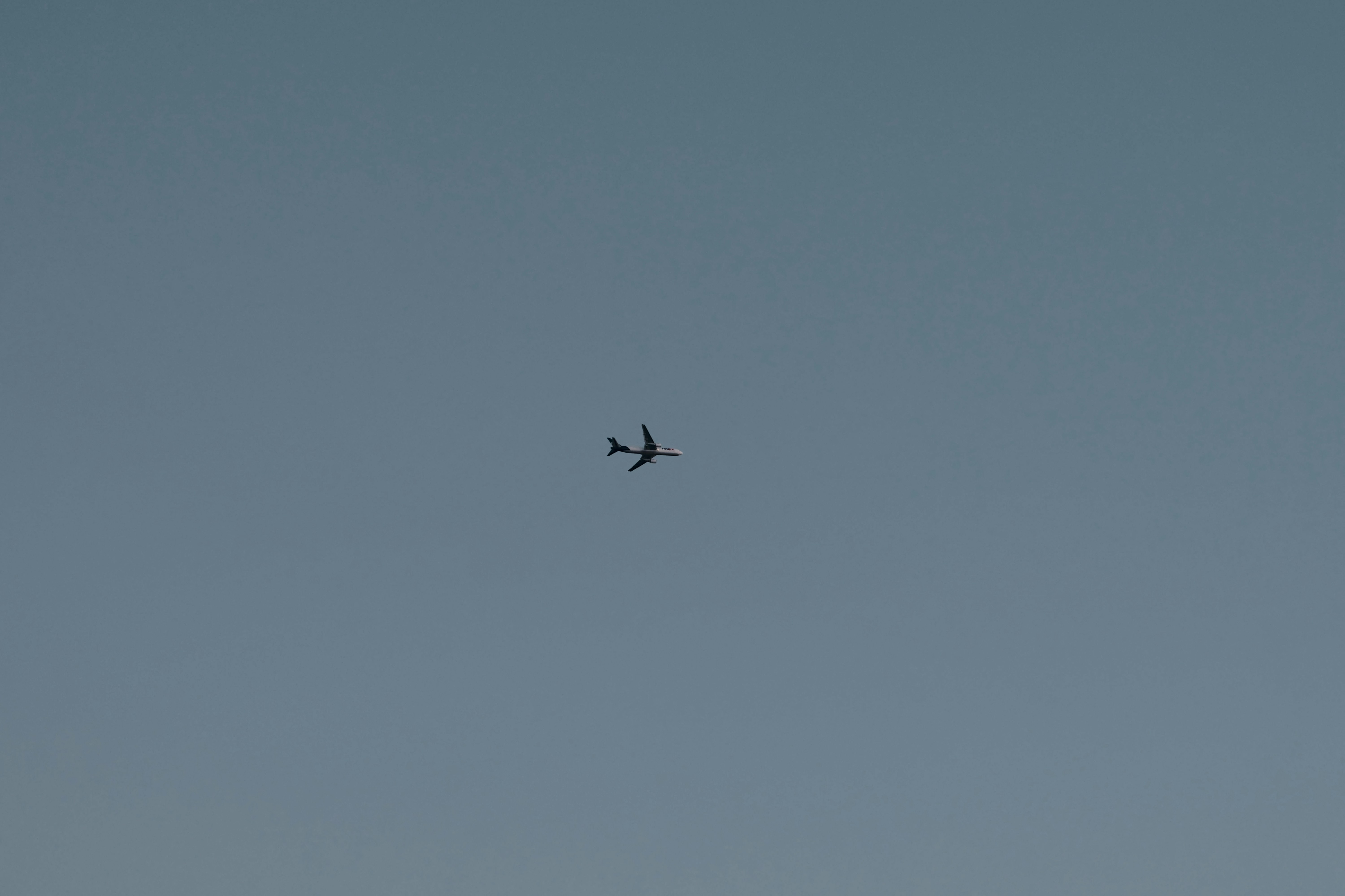 A plane flies high in the clear blue sky.