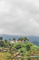 Houses are on a lush, green hillside under cloudy skies.