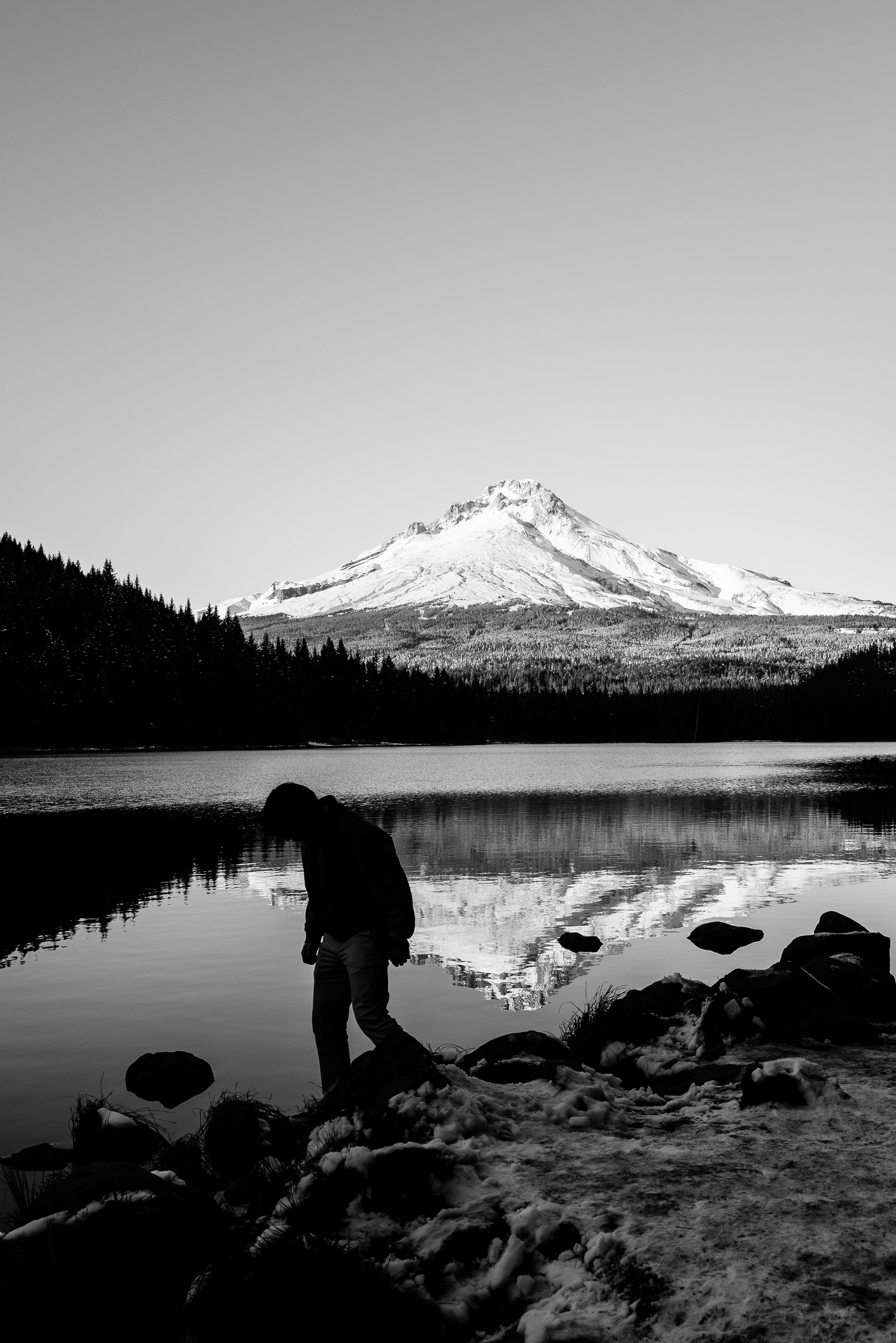 Man stands by a lake with a snowy mountain.