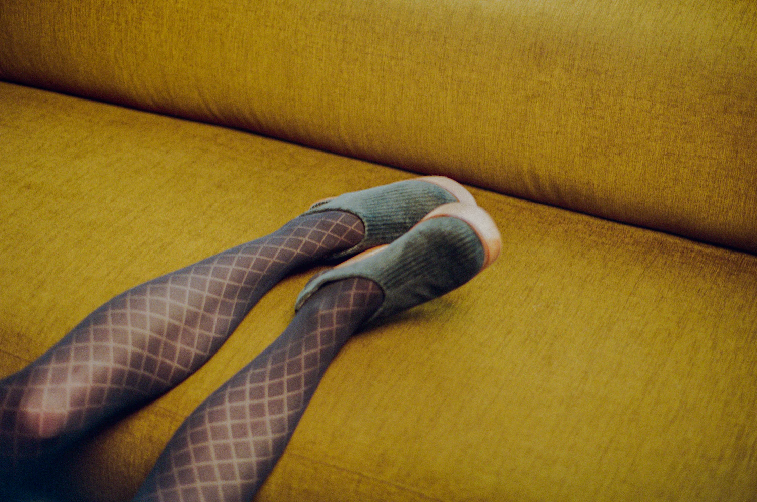 Legs in patterned tights resting on a mustard velvet sofa in daylight
