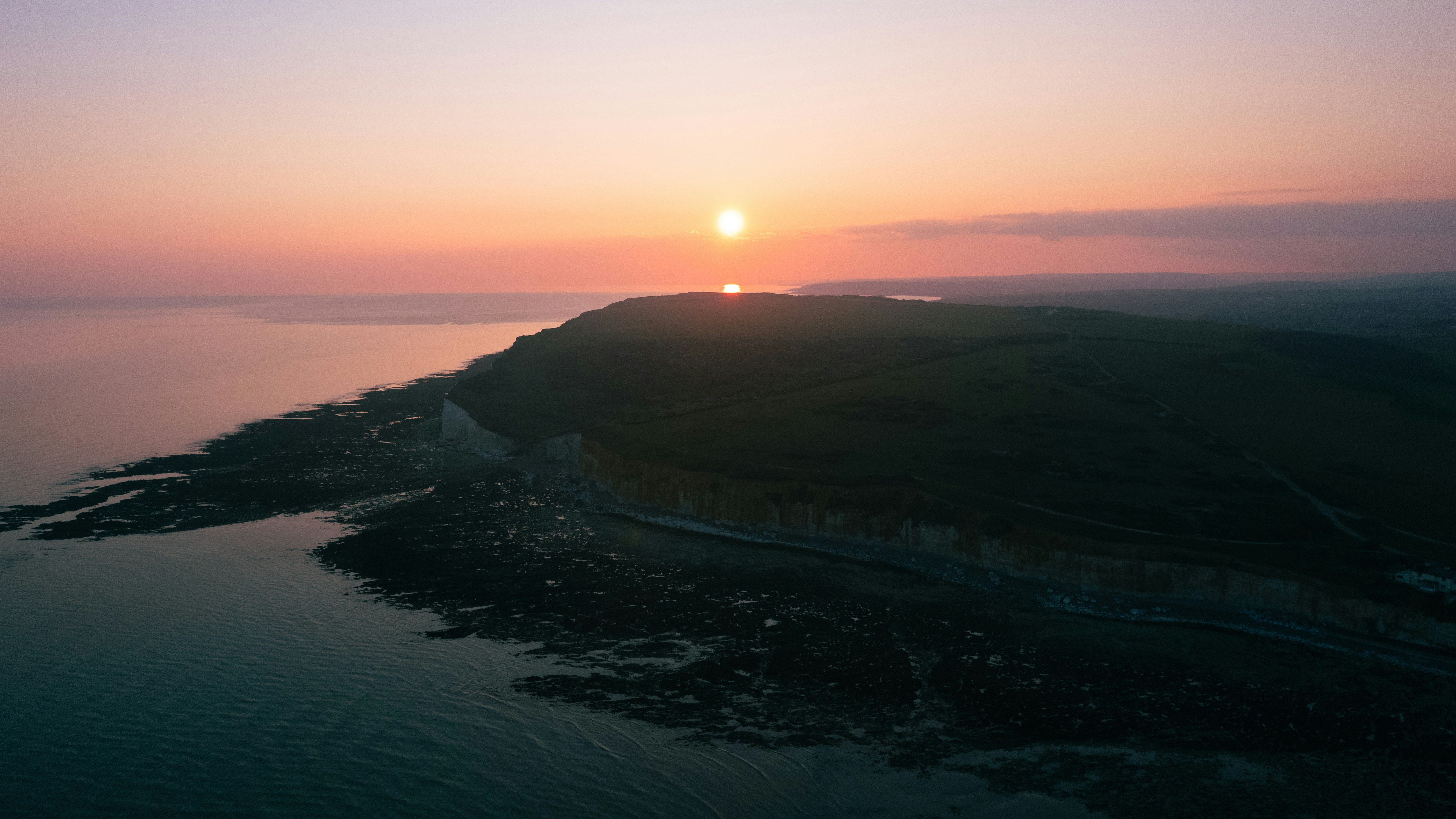 Sunset over a coastline, bathed in soft light.