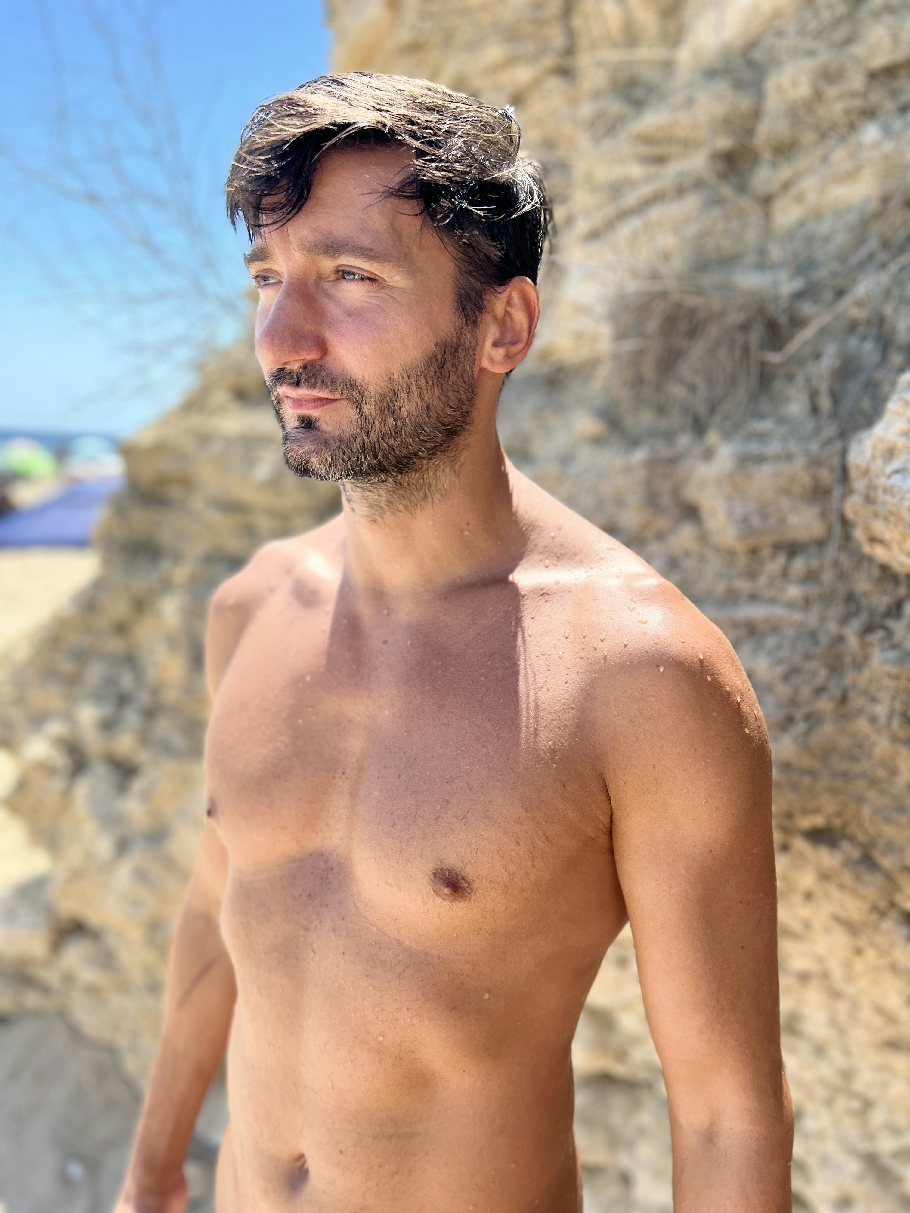 Man poses shirtless near a rocky cliff.