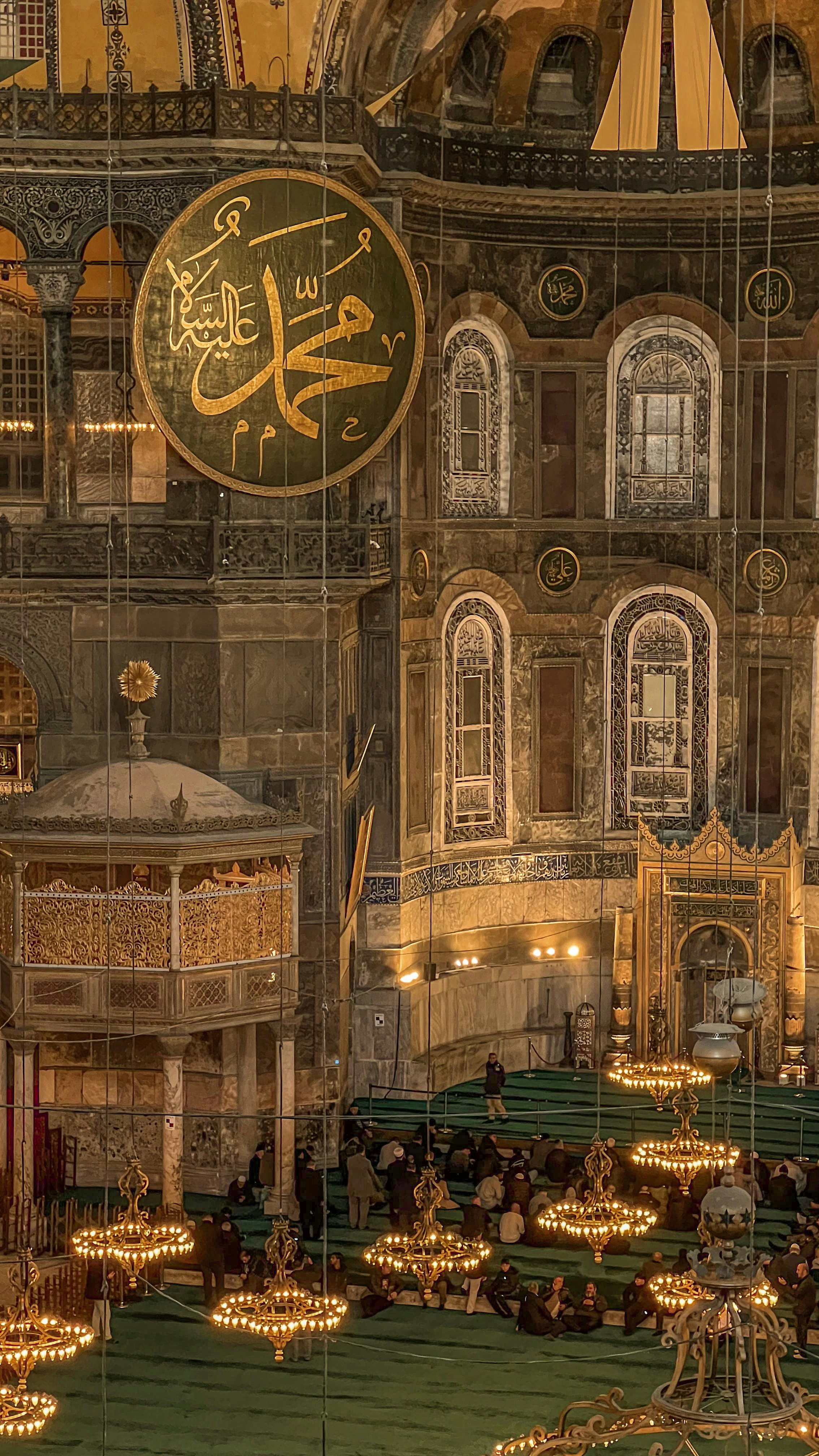 Inside of a mosque with chandeliers and calligraphy.