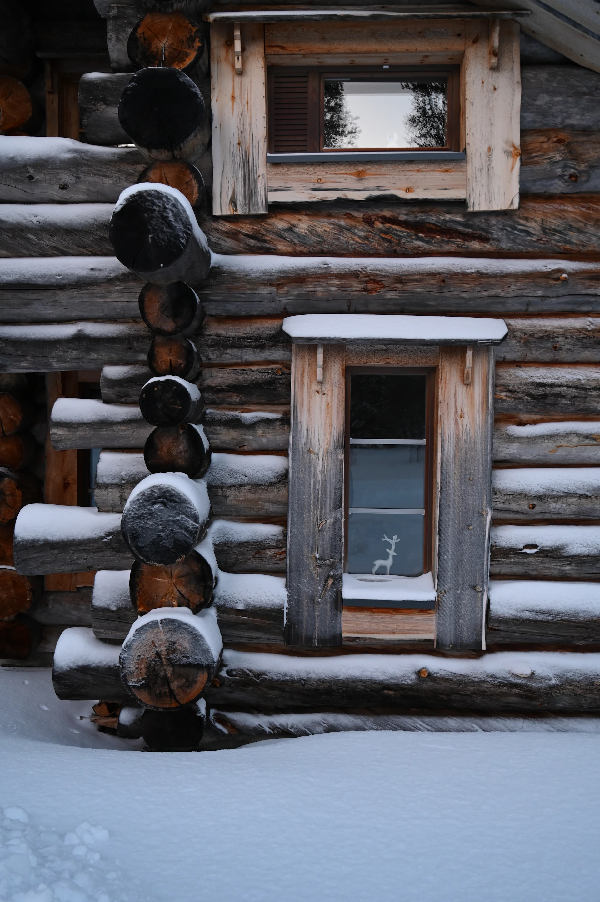 A snowy log cabin with wooden windows.
