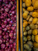 Red onions and potatoes in wooden bins.