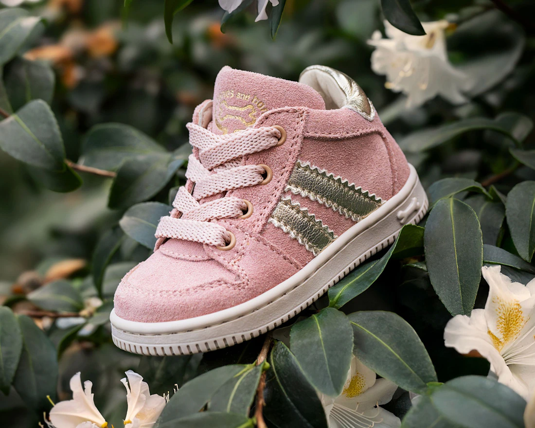 Pink baby sneaker resting among soft green leaves and white flowers