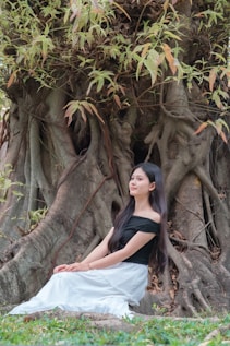 Young woman sits by a large, textured tree.
