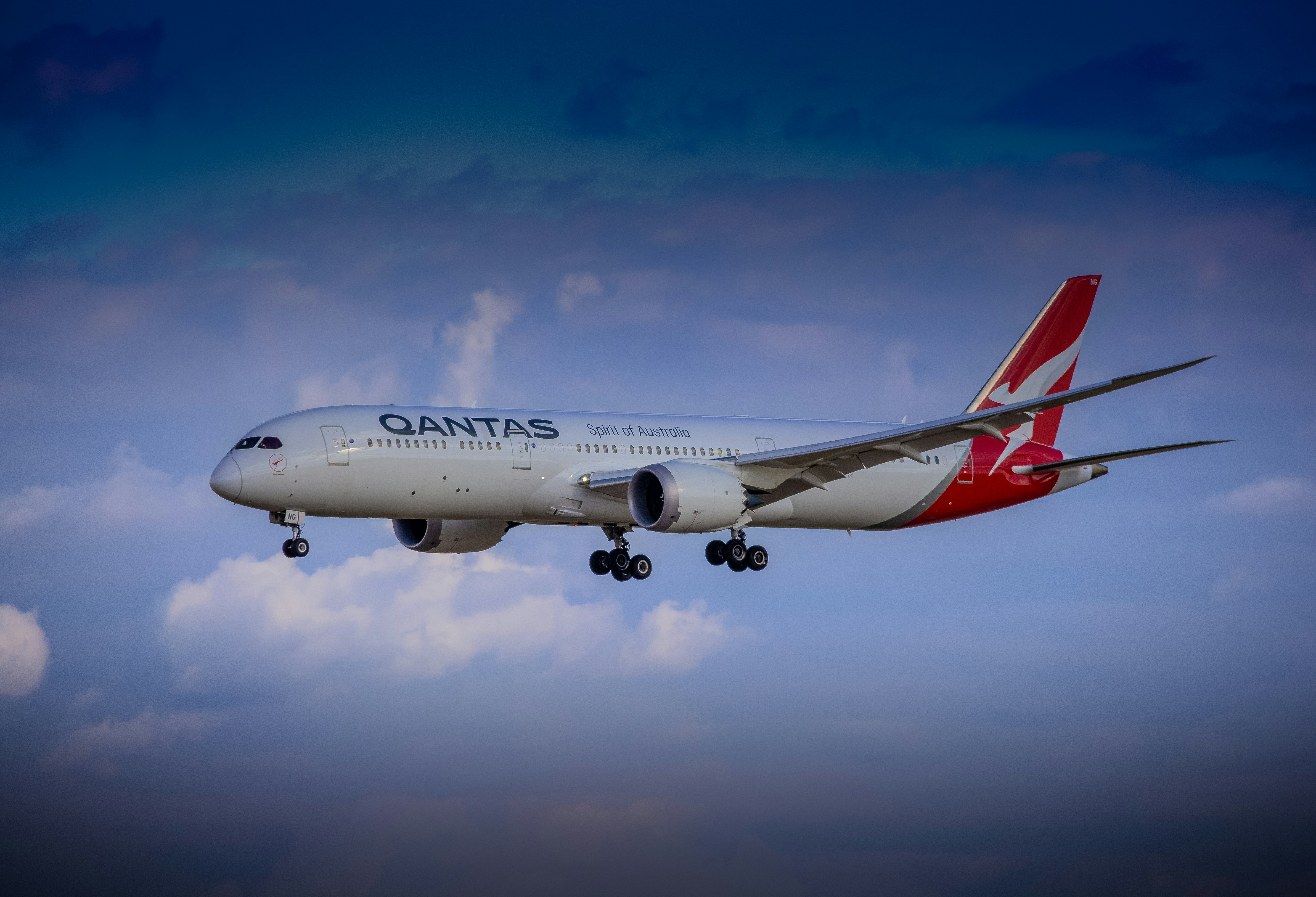 A qantas airplane flies through the cloudy sky.