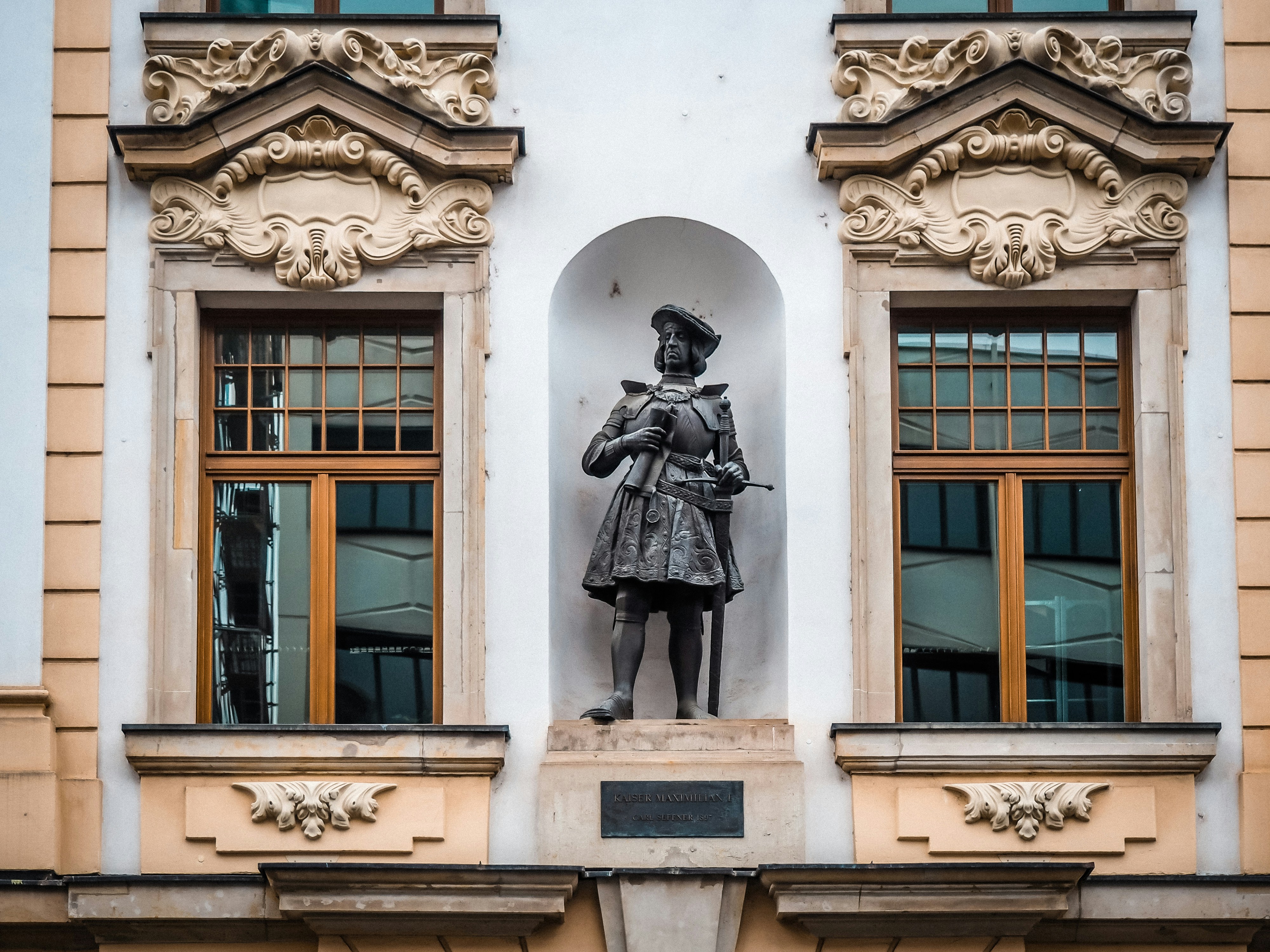 A statue stands between ornate windows.