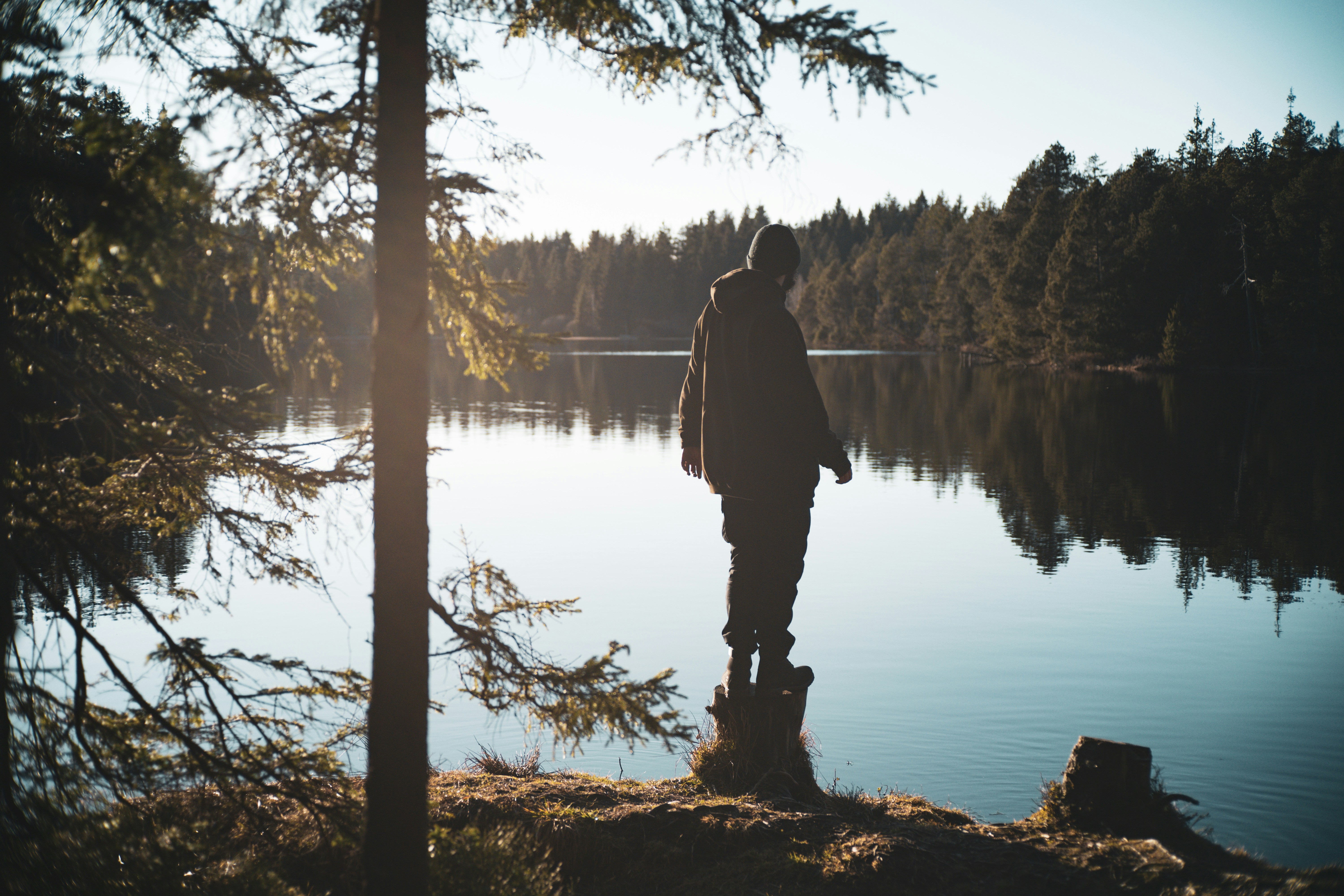 Person stands near a lake surrounded by trees.