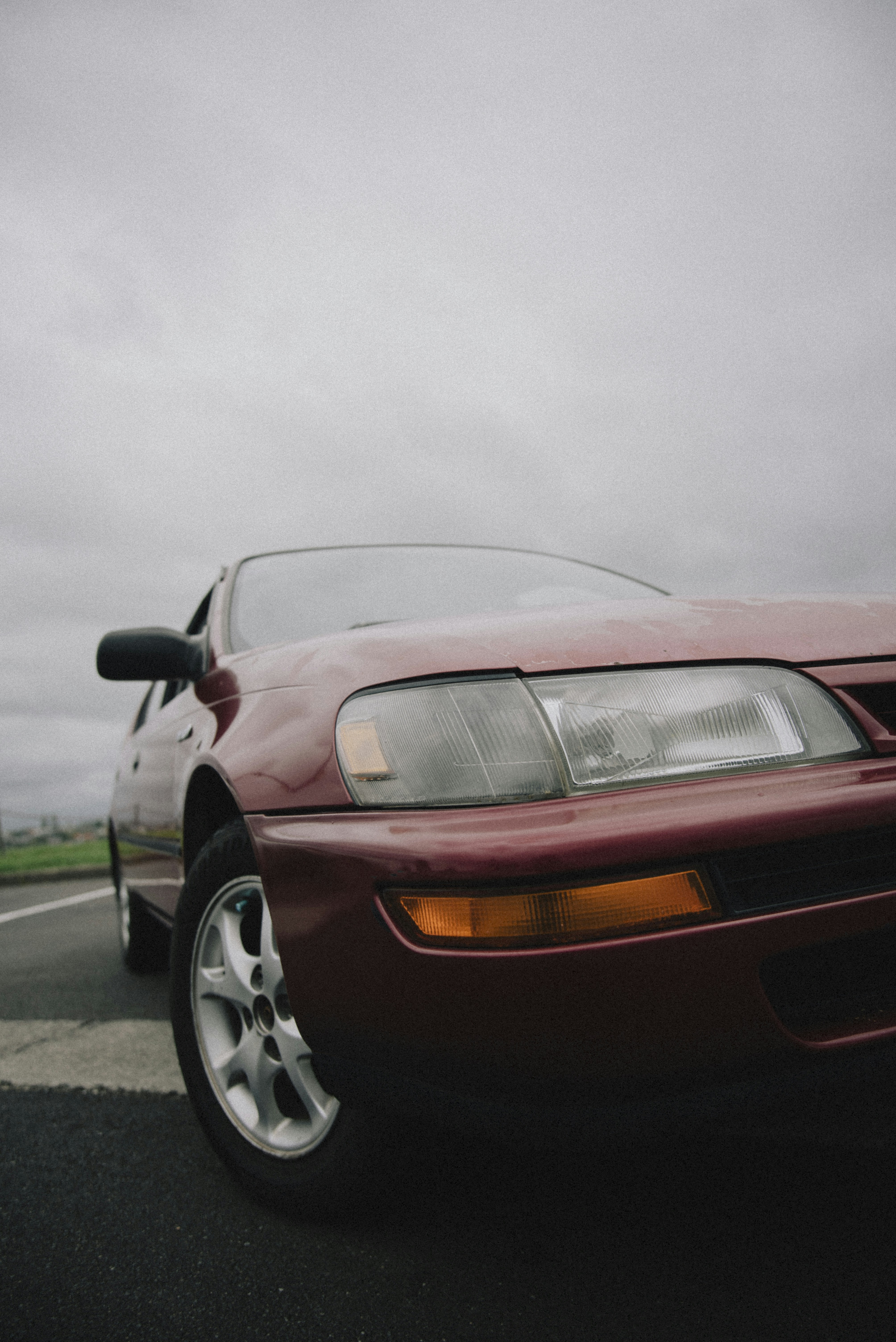 A red car is parked on a cloudy day.