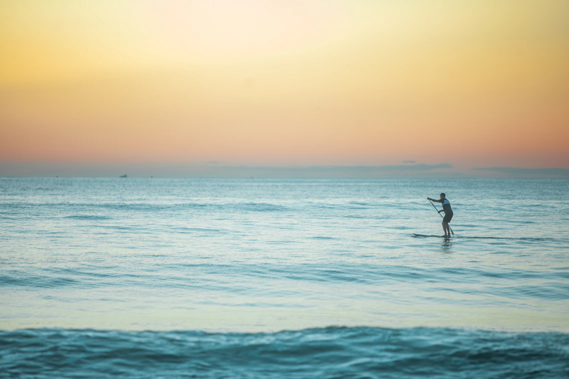 A paddleboarder moving across peaceful ocean water at sunset