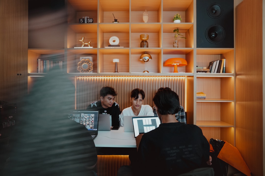Three people working together on their computers., Designers Collaborating in a Warm Wooden Architectural Space