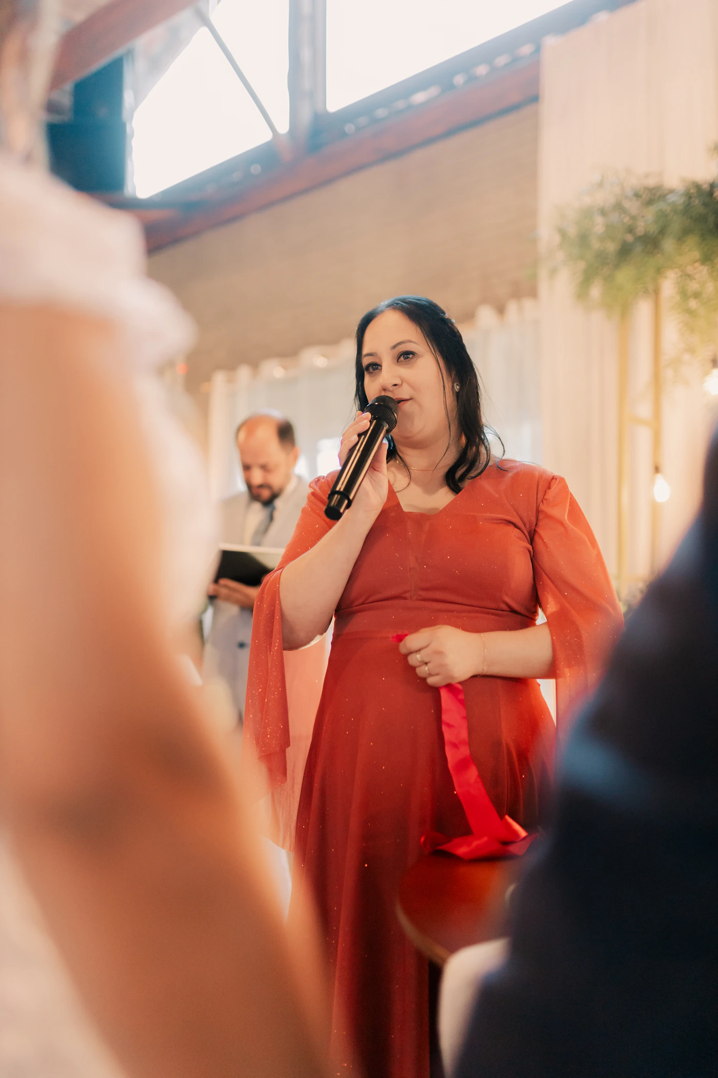 Woman speaking at a wedding ceremony with a microphone showing the toast speaker that most photographers document while missing the couple listening behind them
