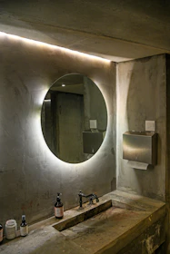 Modern bathroom features a circular, lit-up mirror.