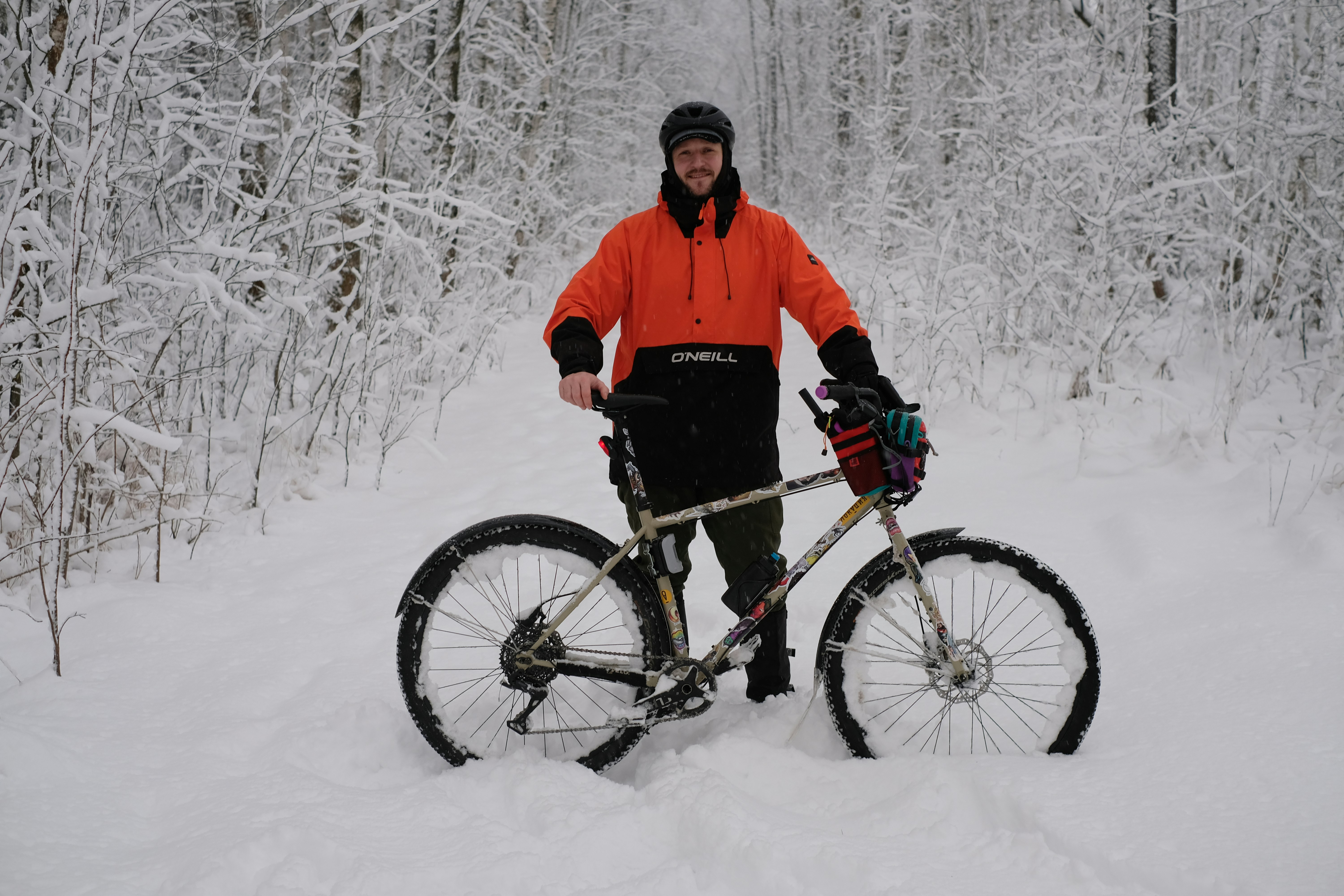 Man poses with his bike in a snowy forest.