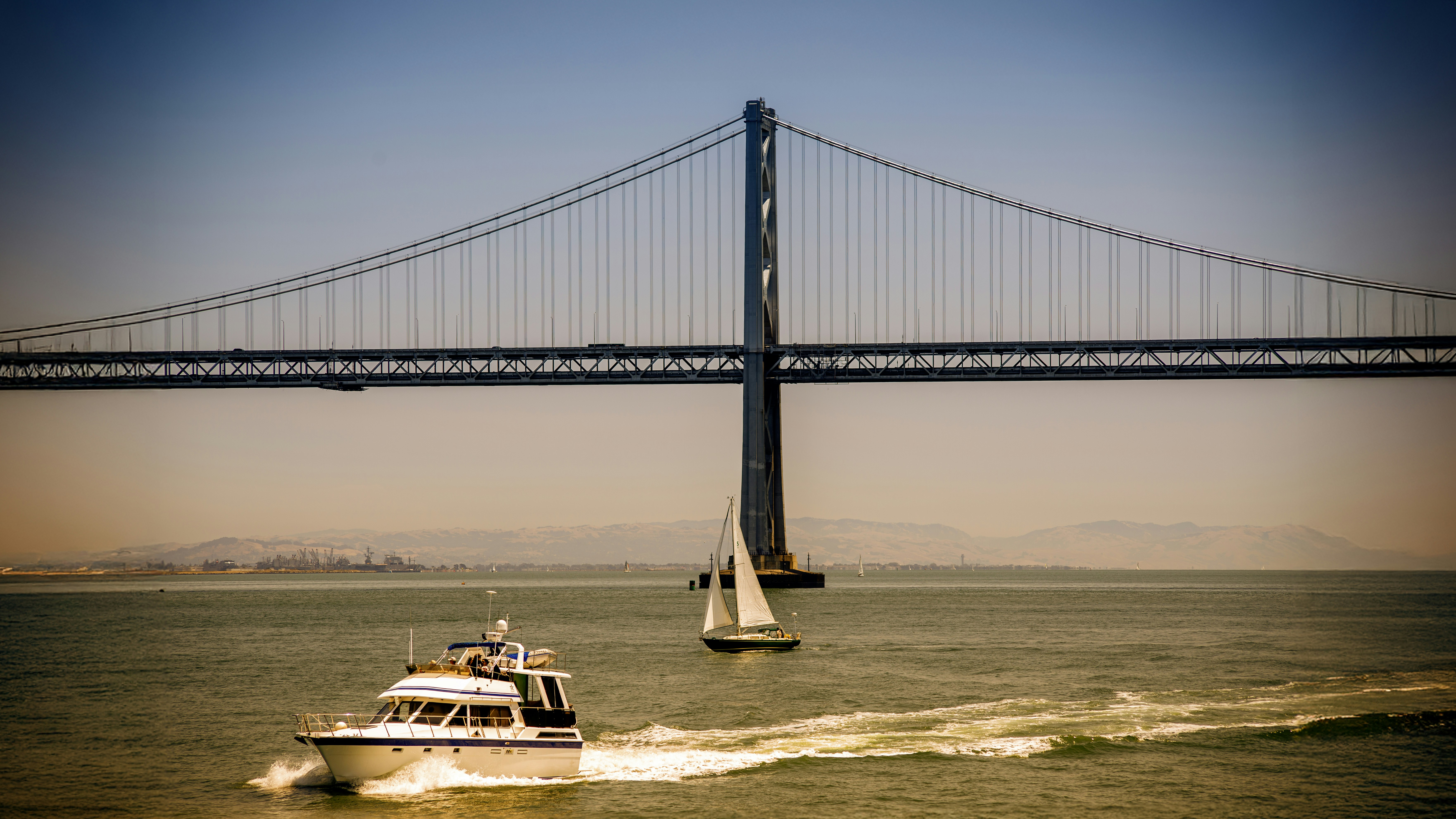 Boats sail under a bridge on the water.