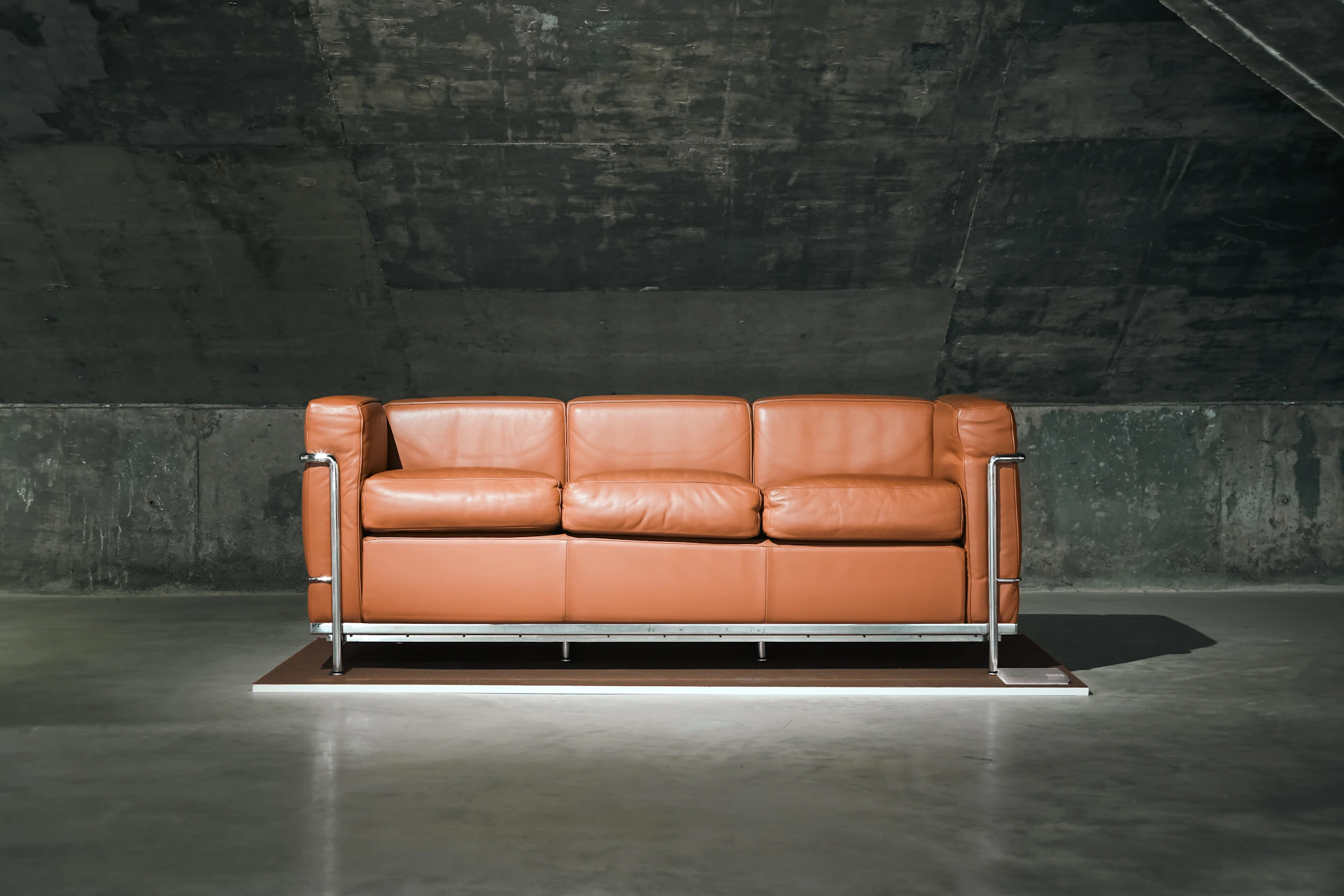 A brown leather sofa sits in a dark room.