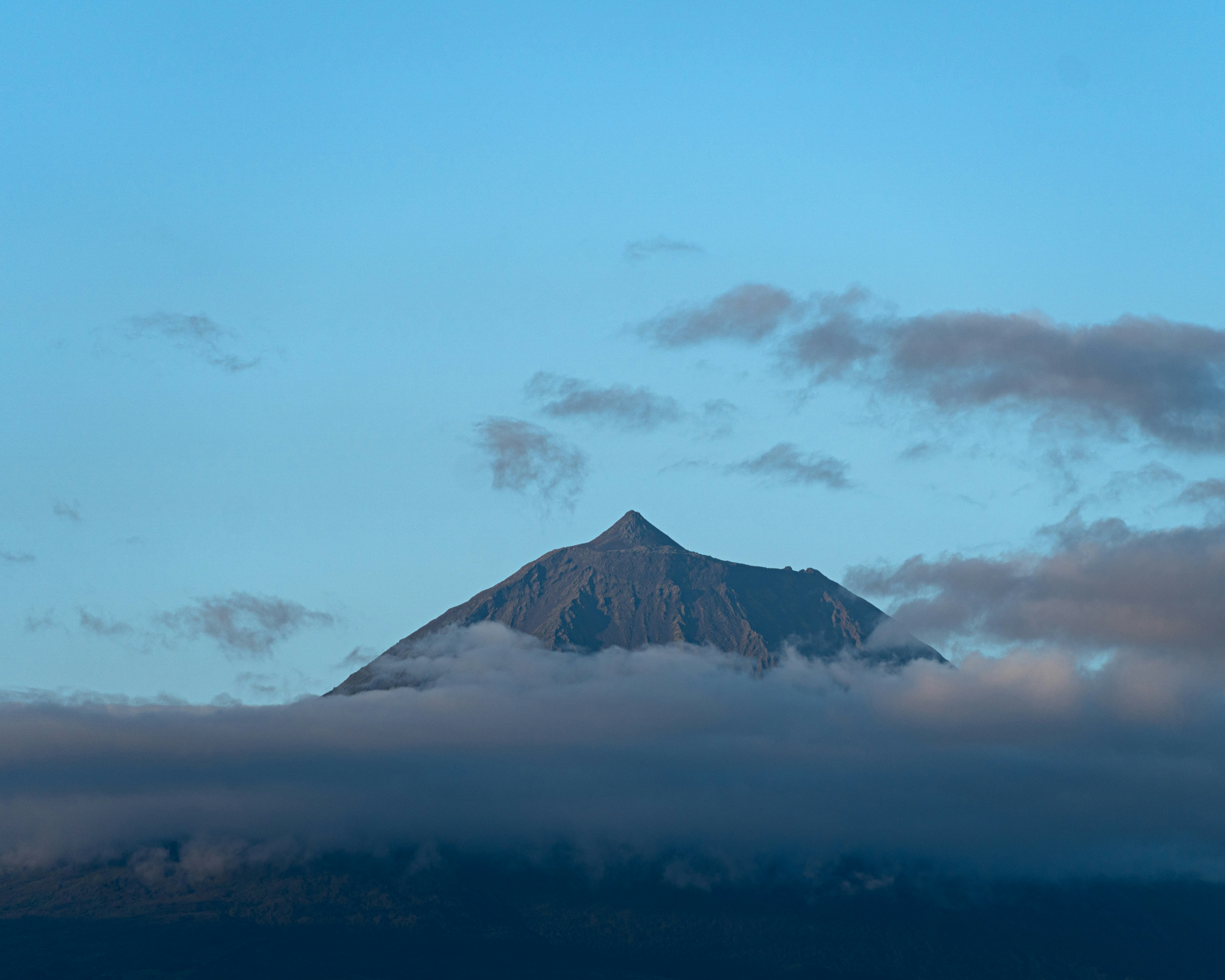 Mountain peak peeking through low clouds and sky.