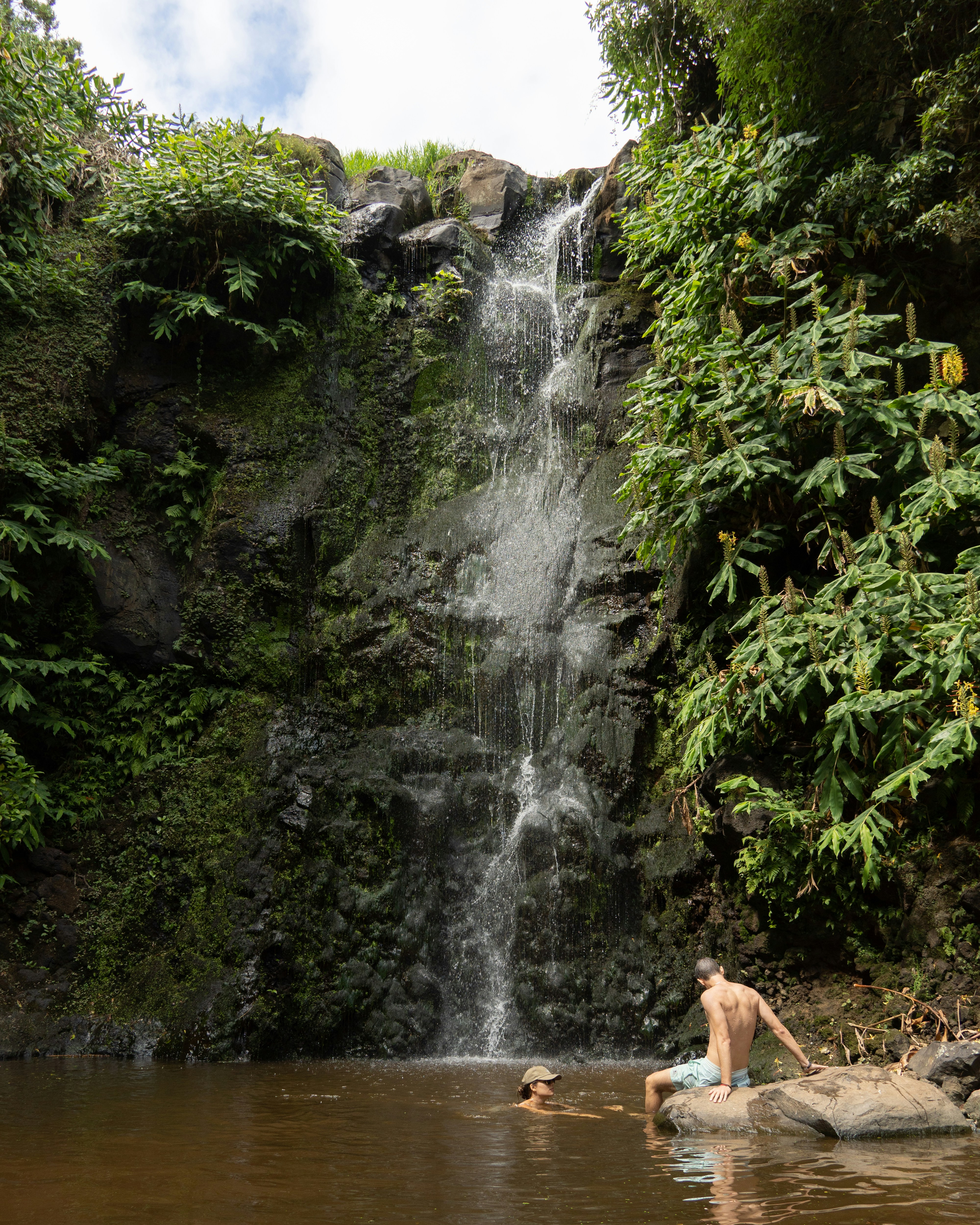 People swim and enjoy the waterfall.