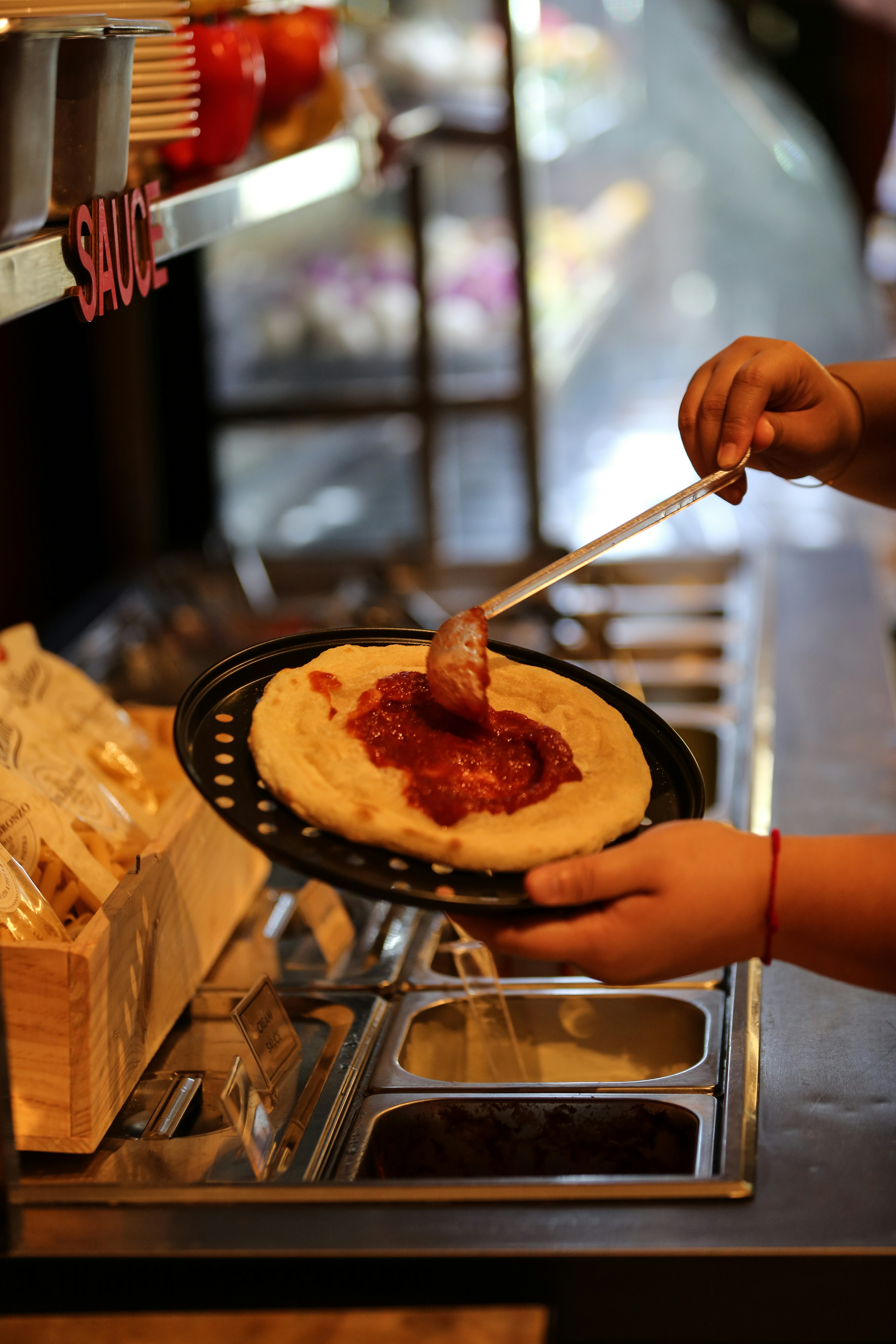 Someone is putting sauce on a pizza crust.