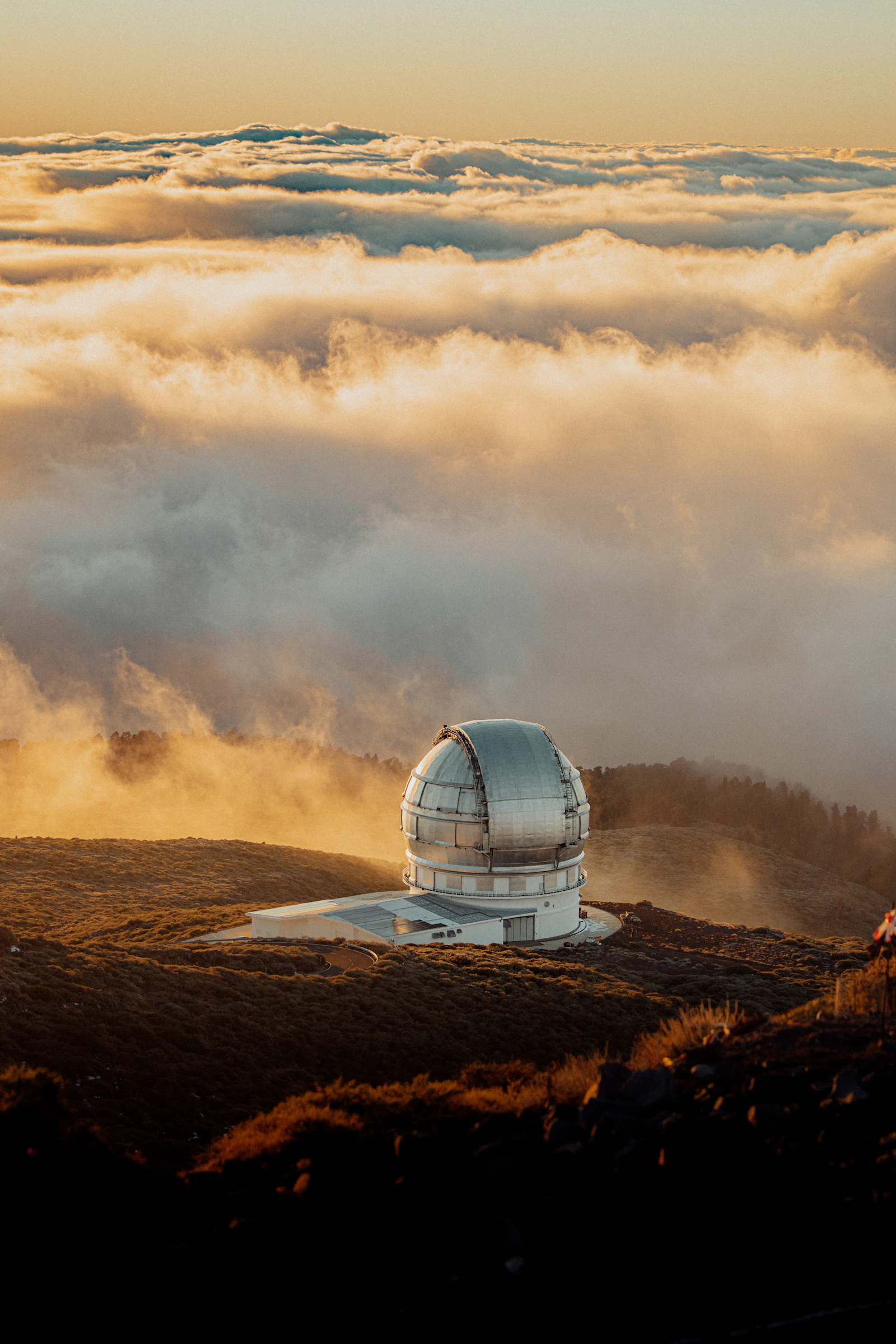 A telescope observatory overlooking clouds at sunset