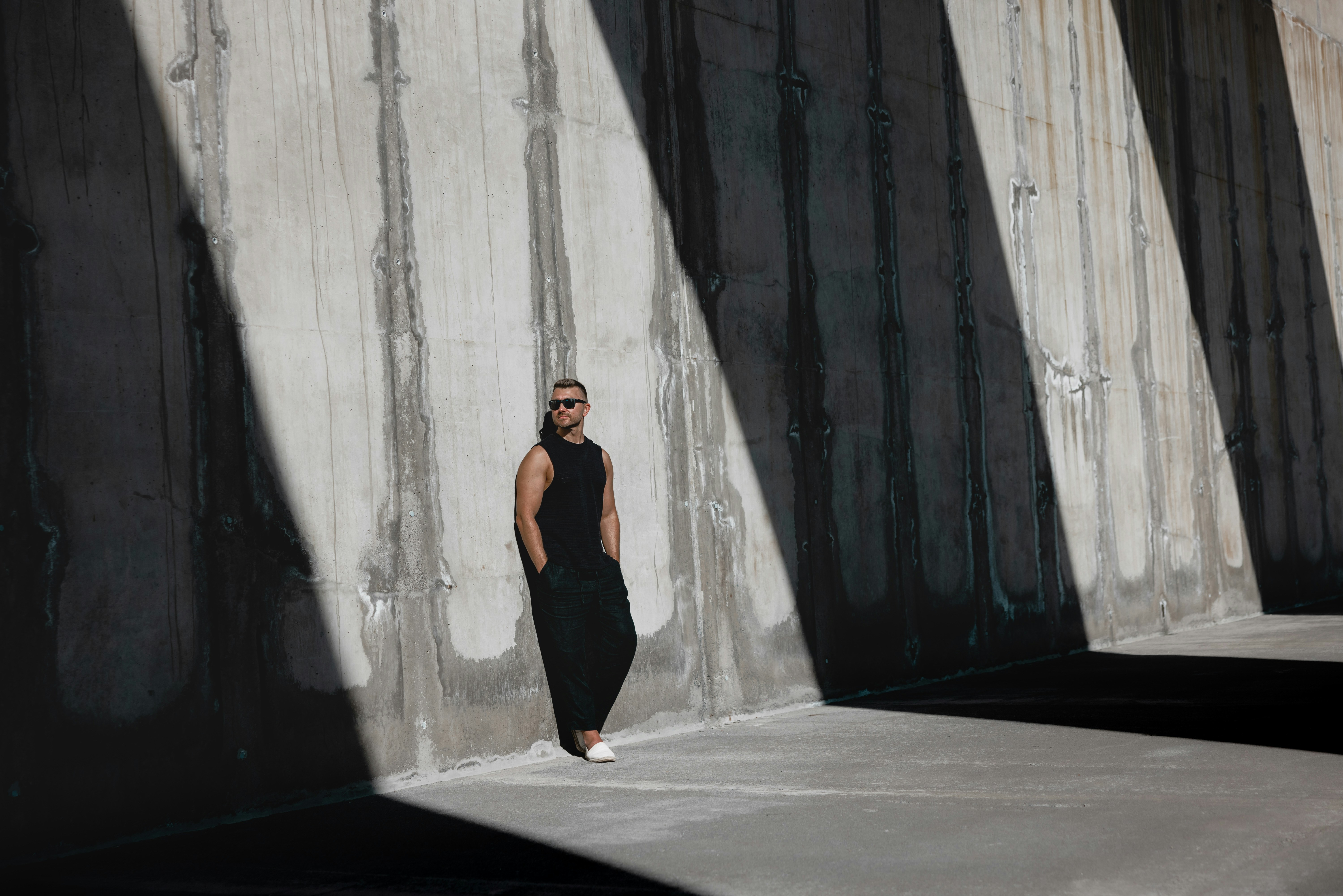 A man poses against a concrete wall.