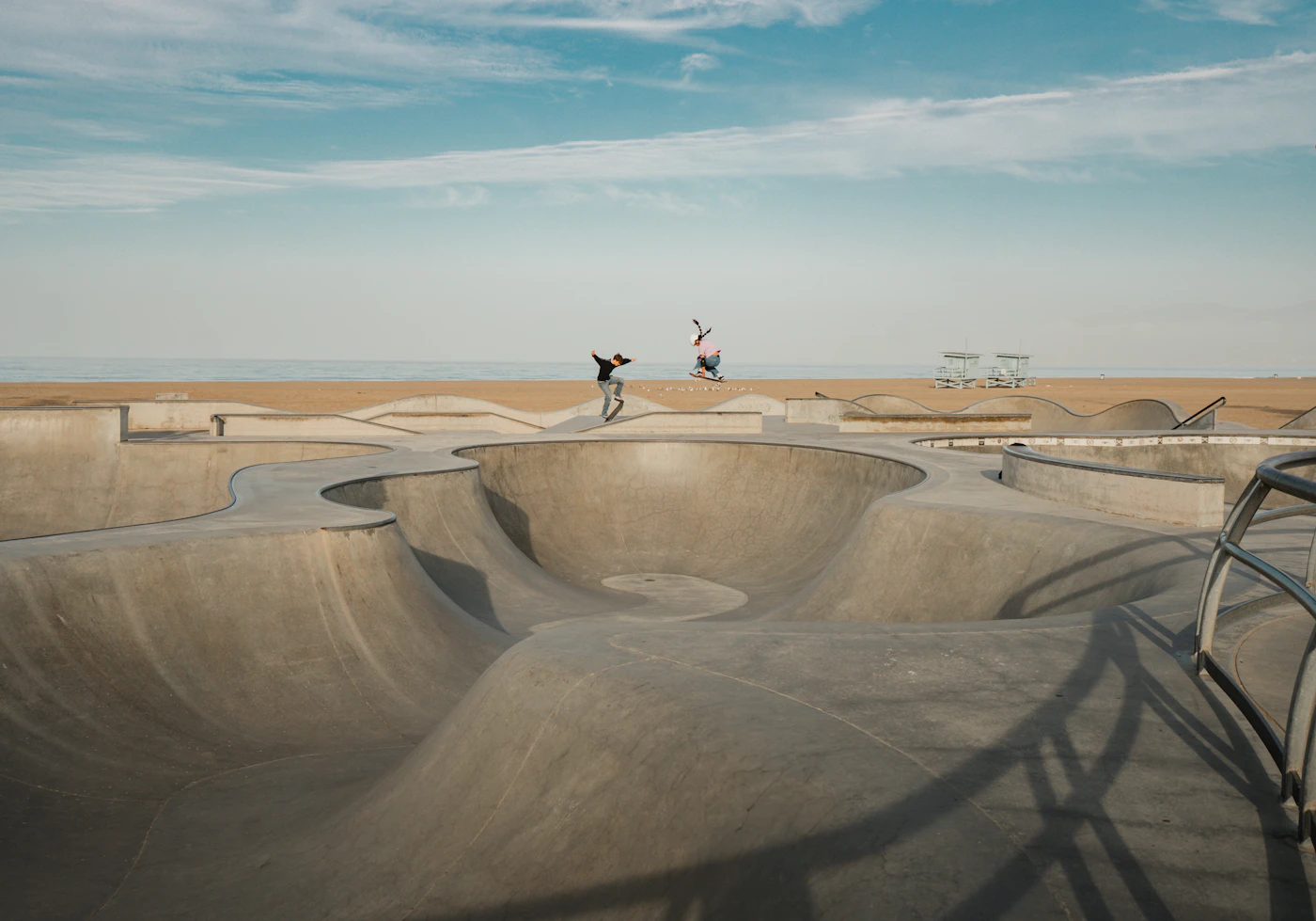 Two skateboarders riding a concrete skatepark on a sunny day