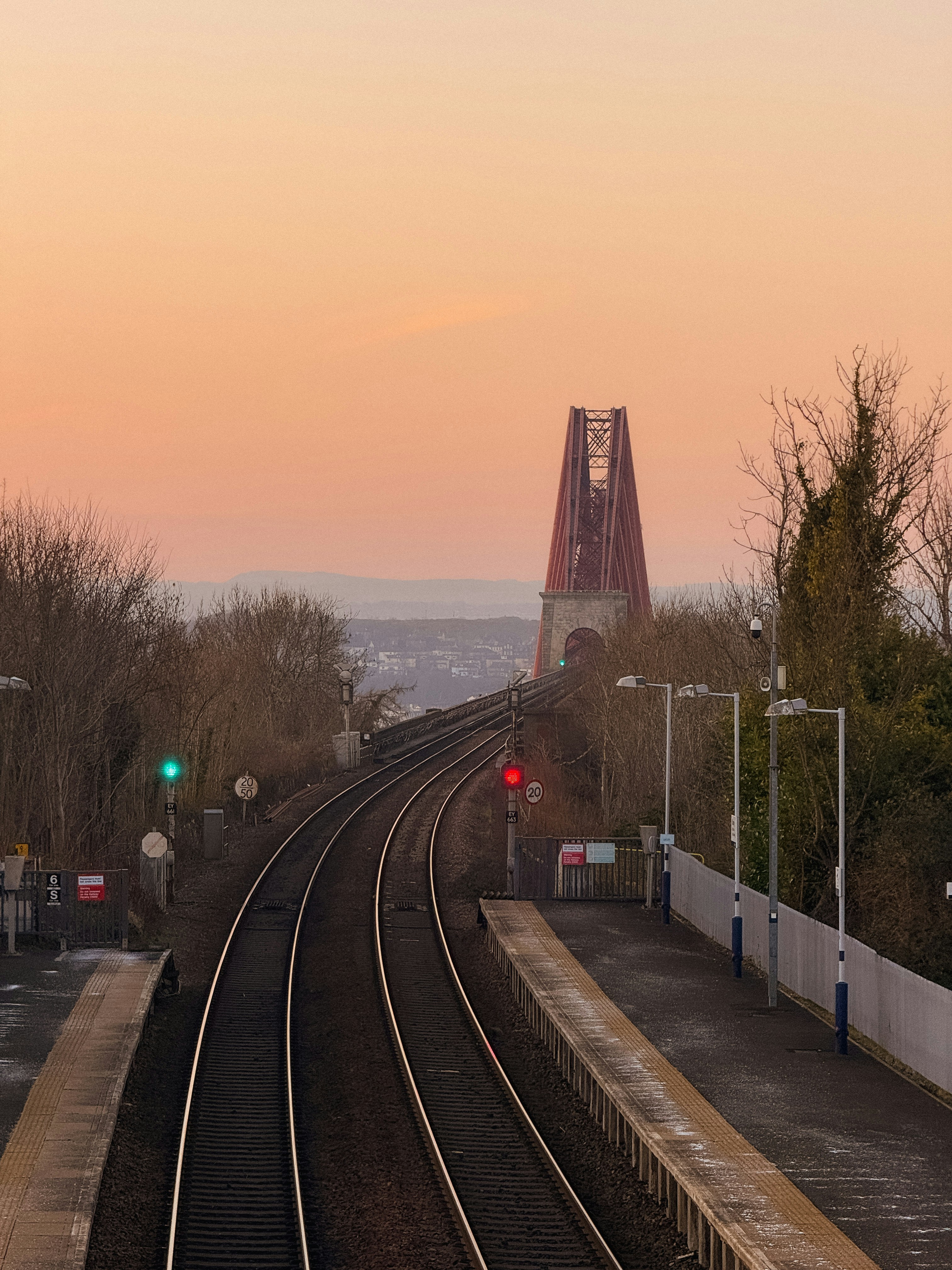 Railway tracks leading towards a bridge at sunset.