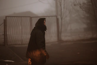 Woman walks in a foggy, somber scene.