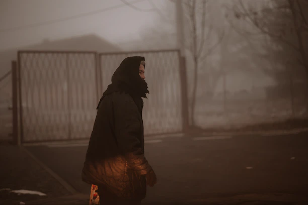 Woman walks in a foggy, somber scene.