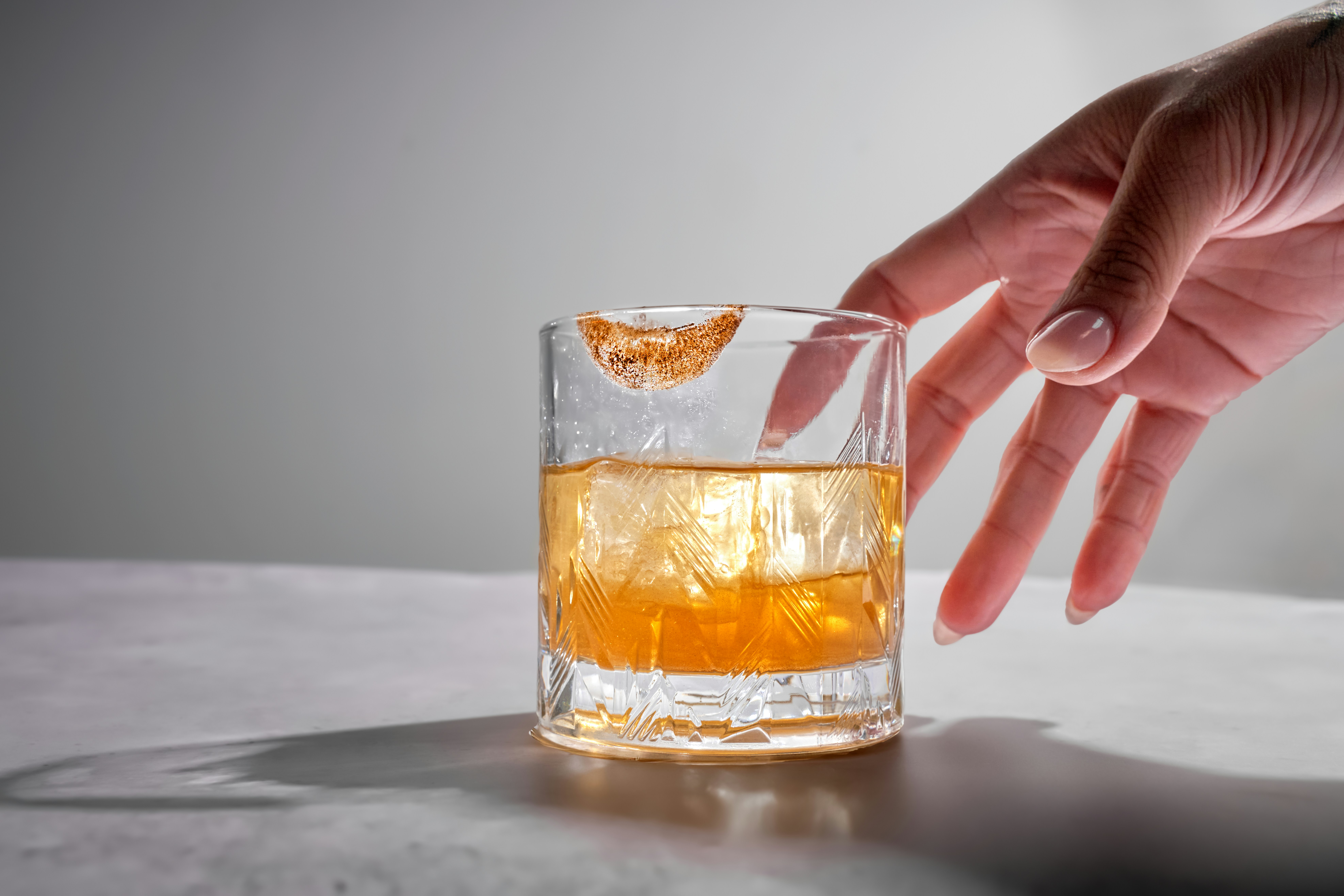 Hand reaching for an amber cocktail on a white bar