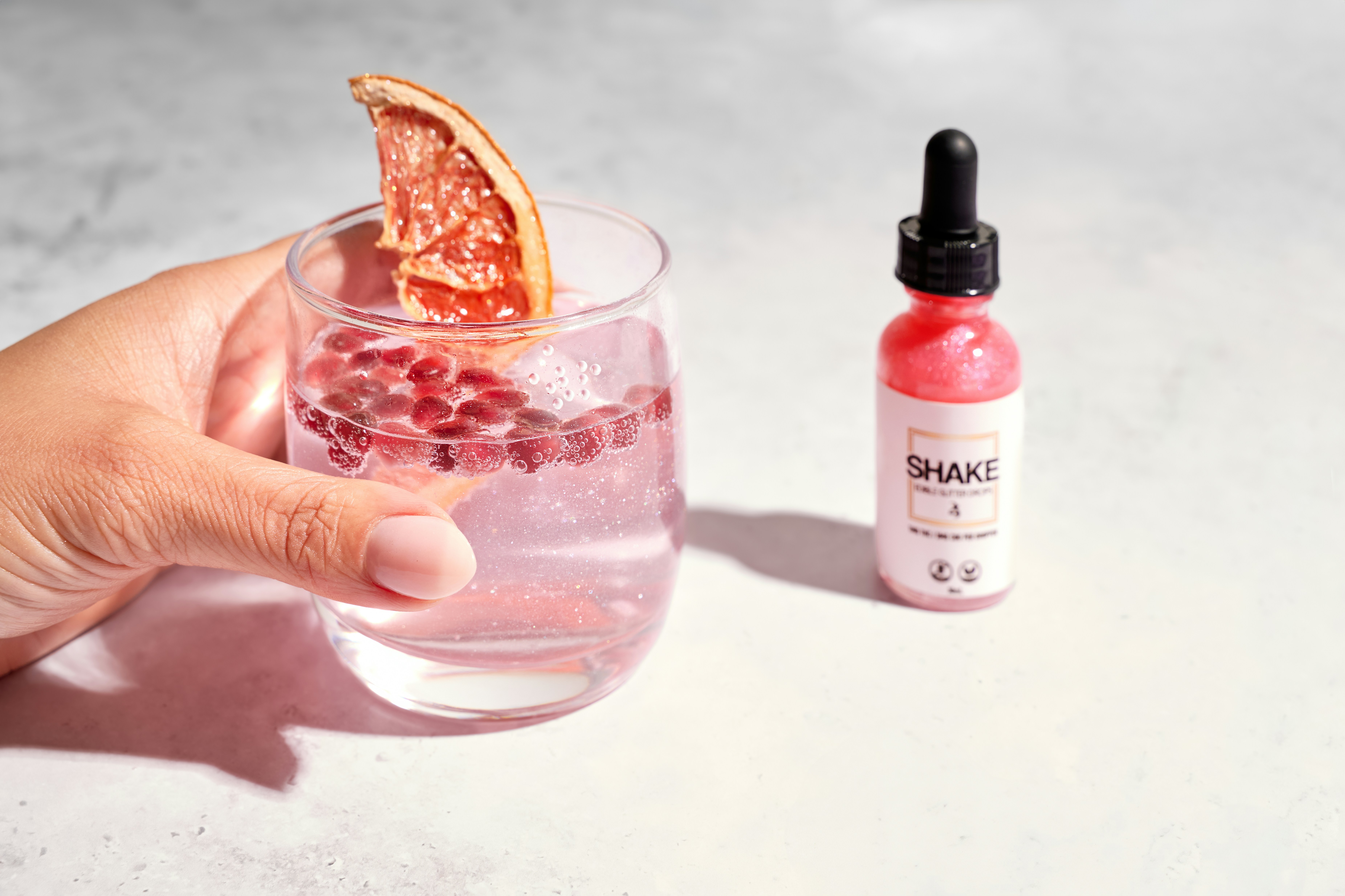 A hand holds a pink cocktail with a dried citrus garnish.
