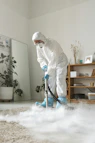 A person in protective suit cleans a carpet.