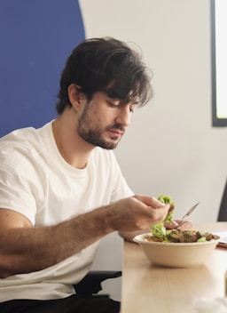 Man eats salad at a table indoors.