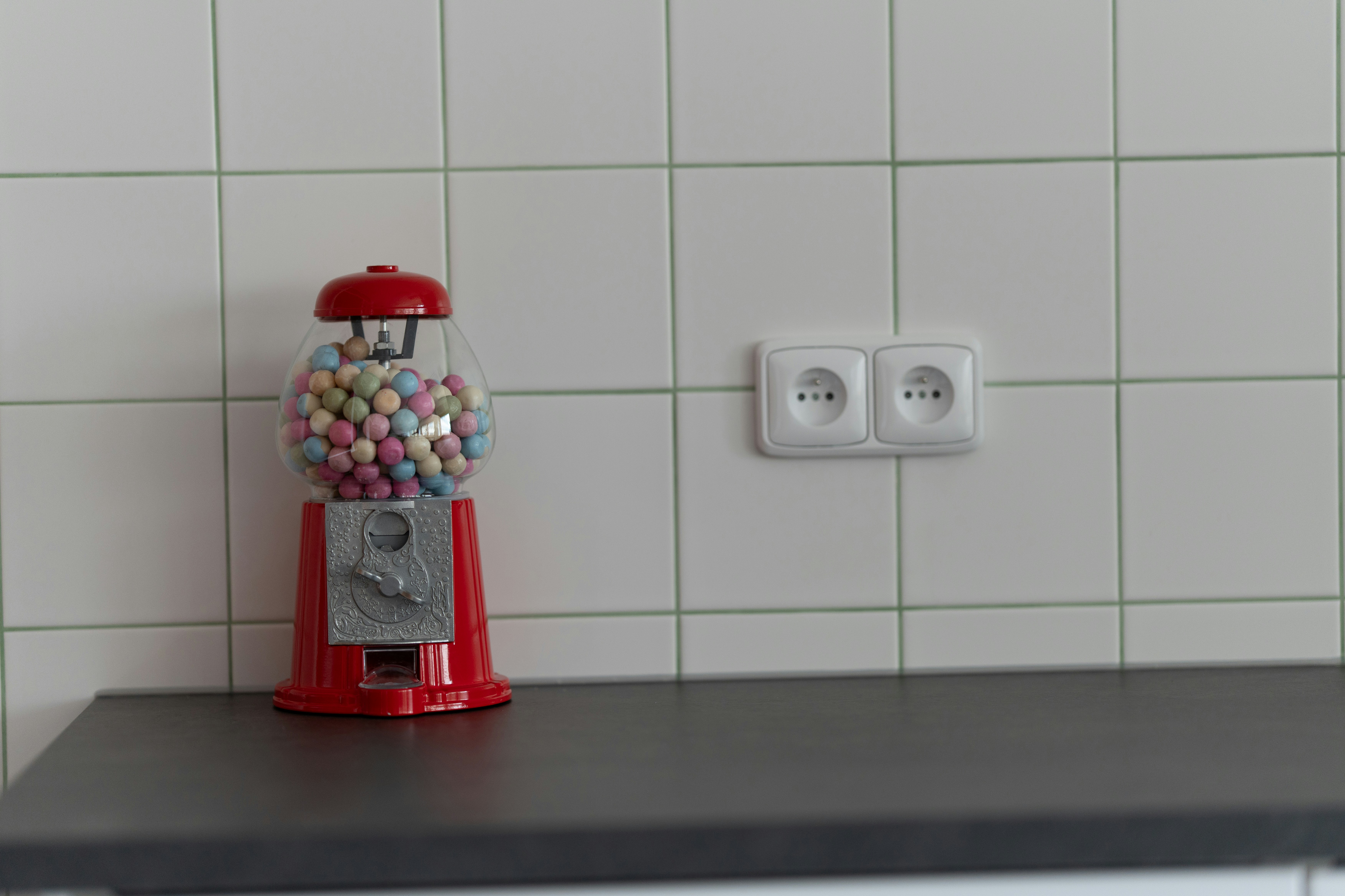 A gumball machine stands next to an electrical outlet.