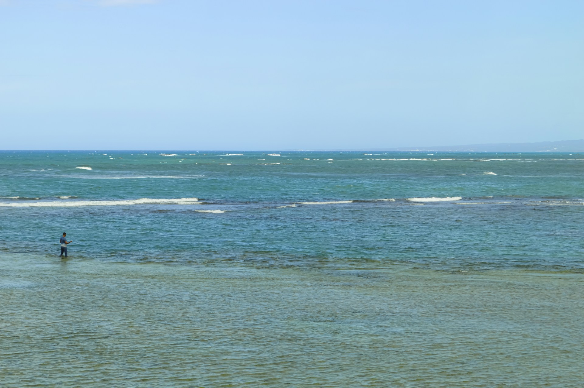 Man fishes in the calm, turquoise ocean.