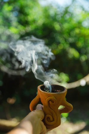 Hand holds a smoking, decorative clay incense burner.