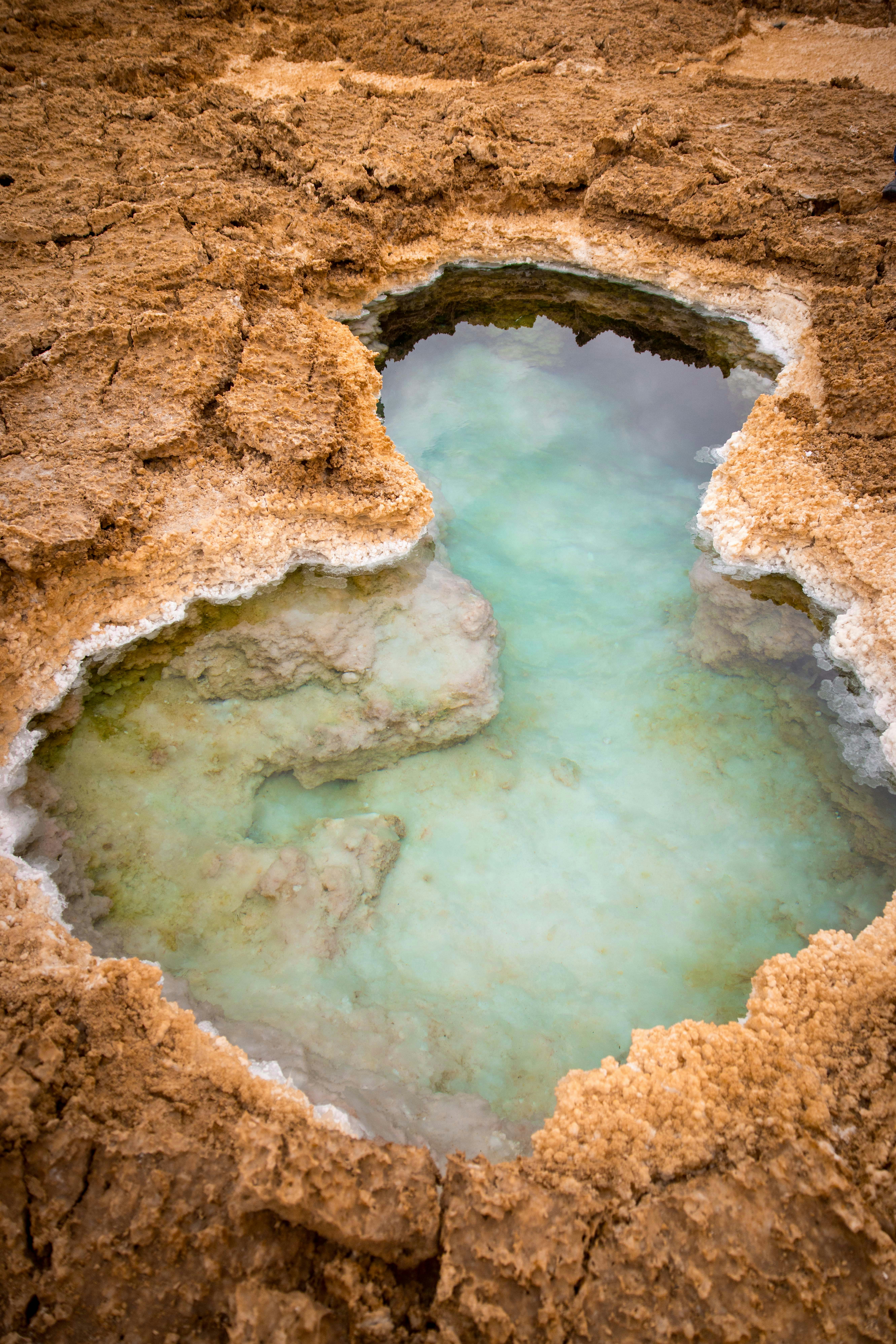 A turquoise pool lies in a brown, cracked landscape.