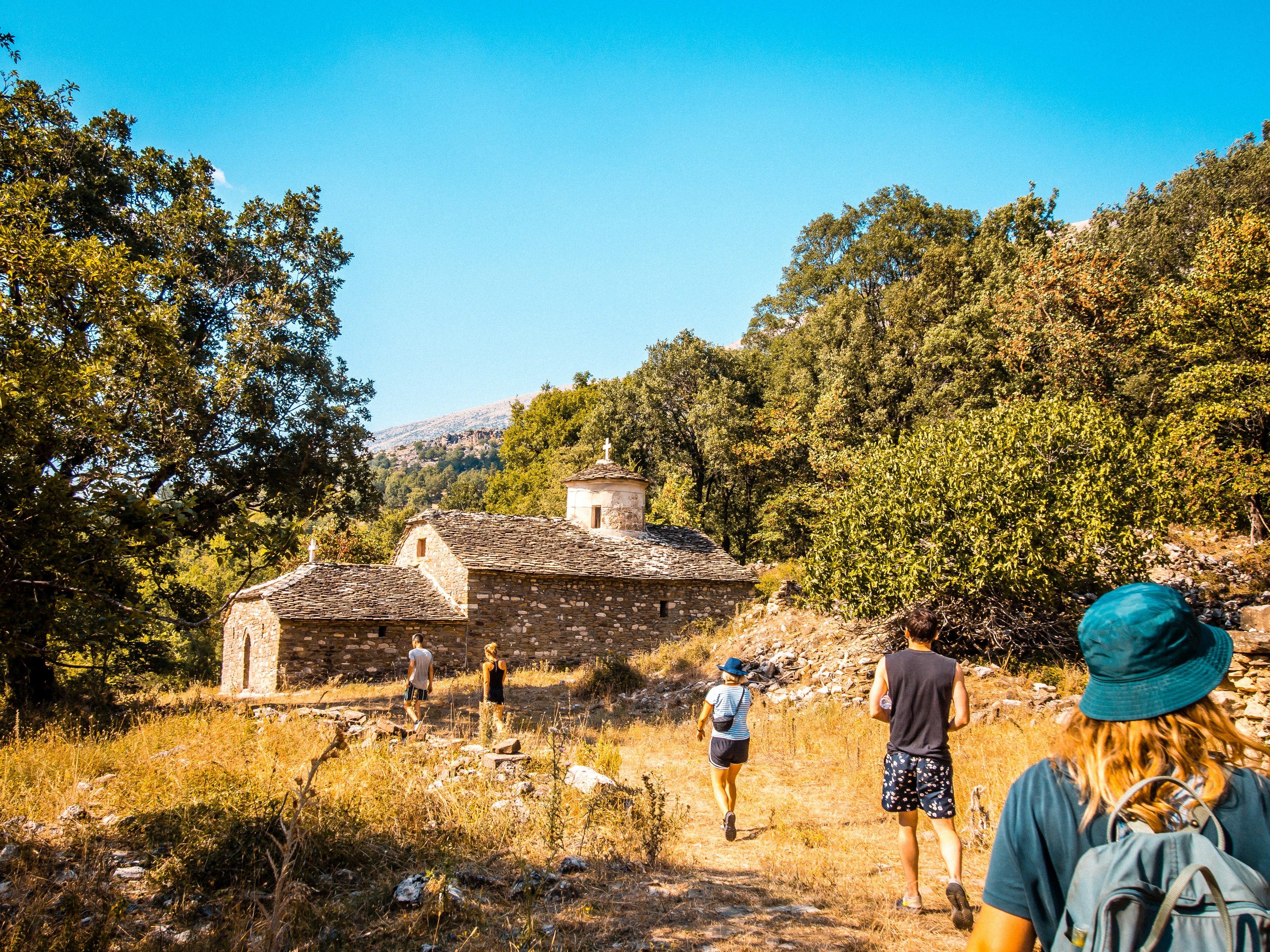 People hike toward an old building in nature.