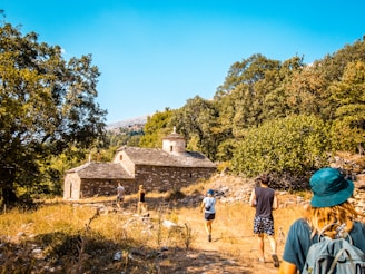 People hike toward an old building in nature.