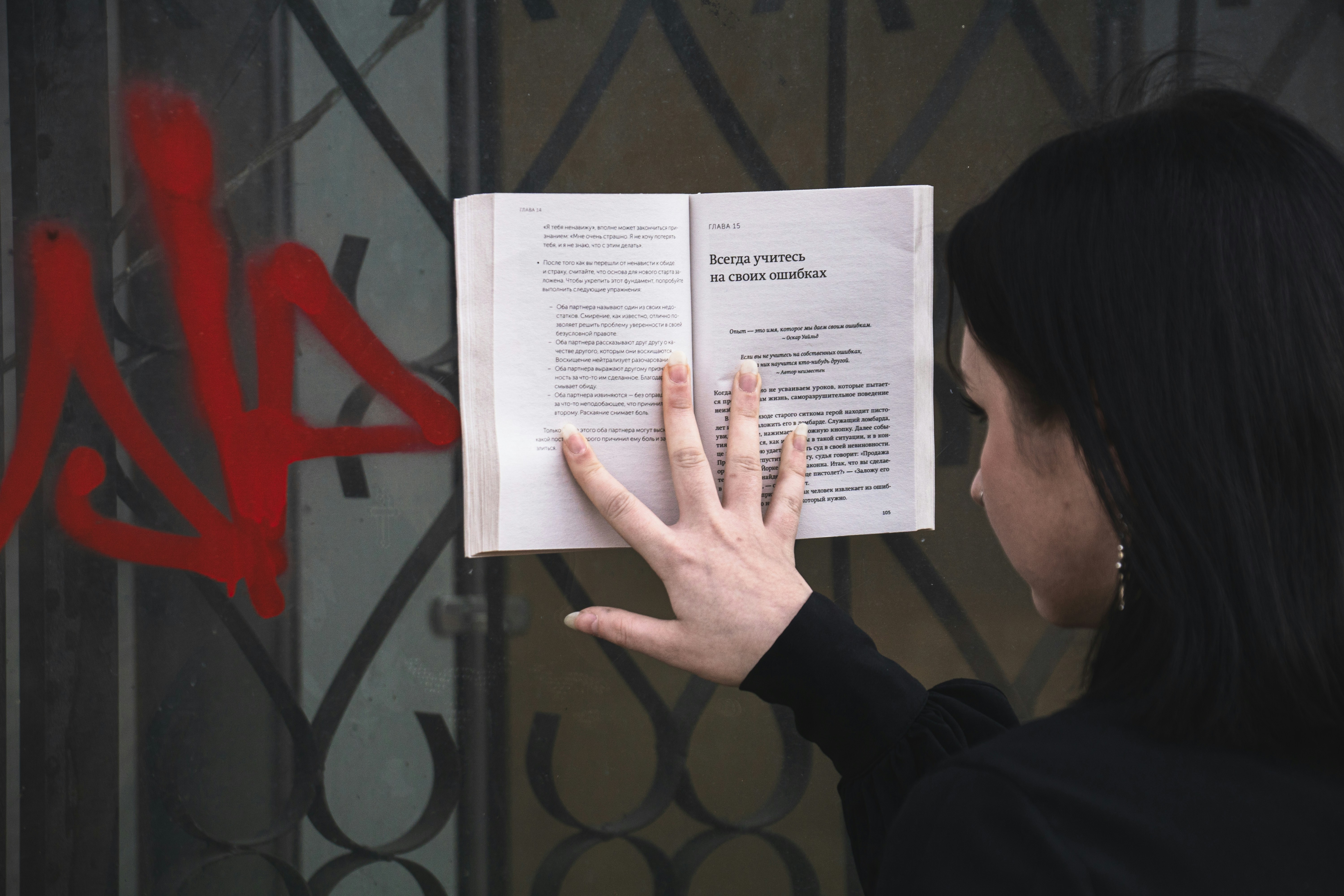Woman reads a book attached to a metal gate.