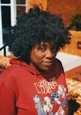 A person in a red hoodie is looking at the camera.