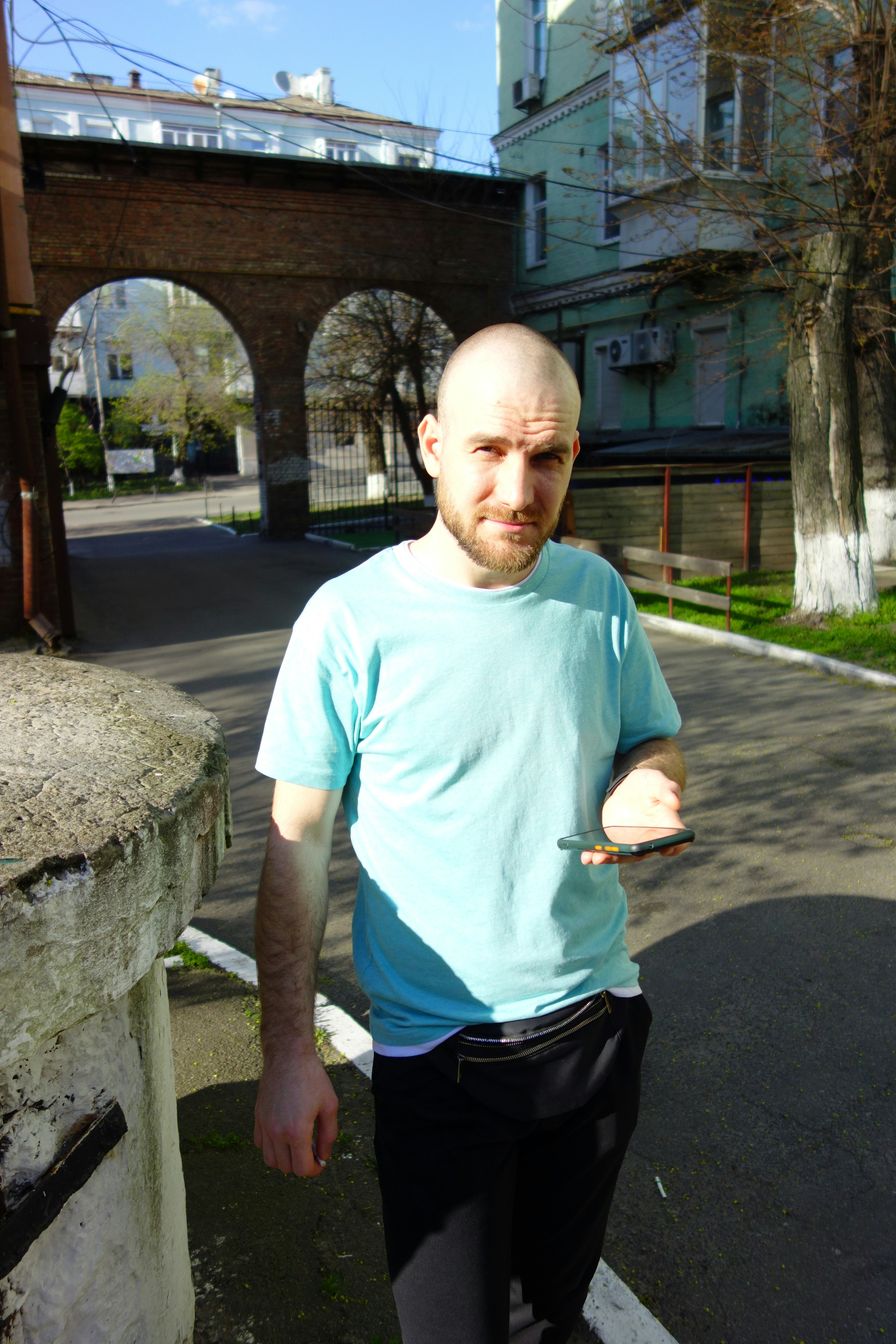 Man poses with a phone near a brick archway.
