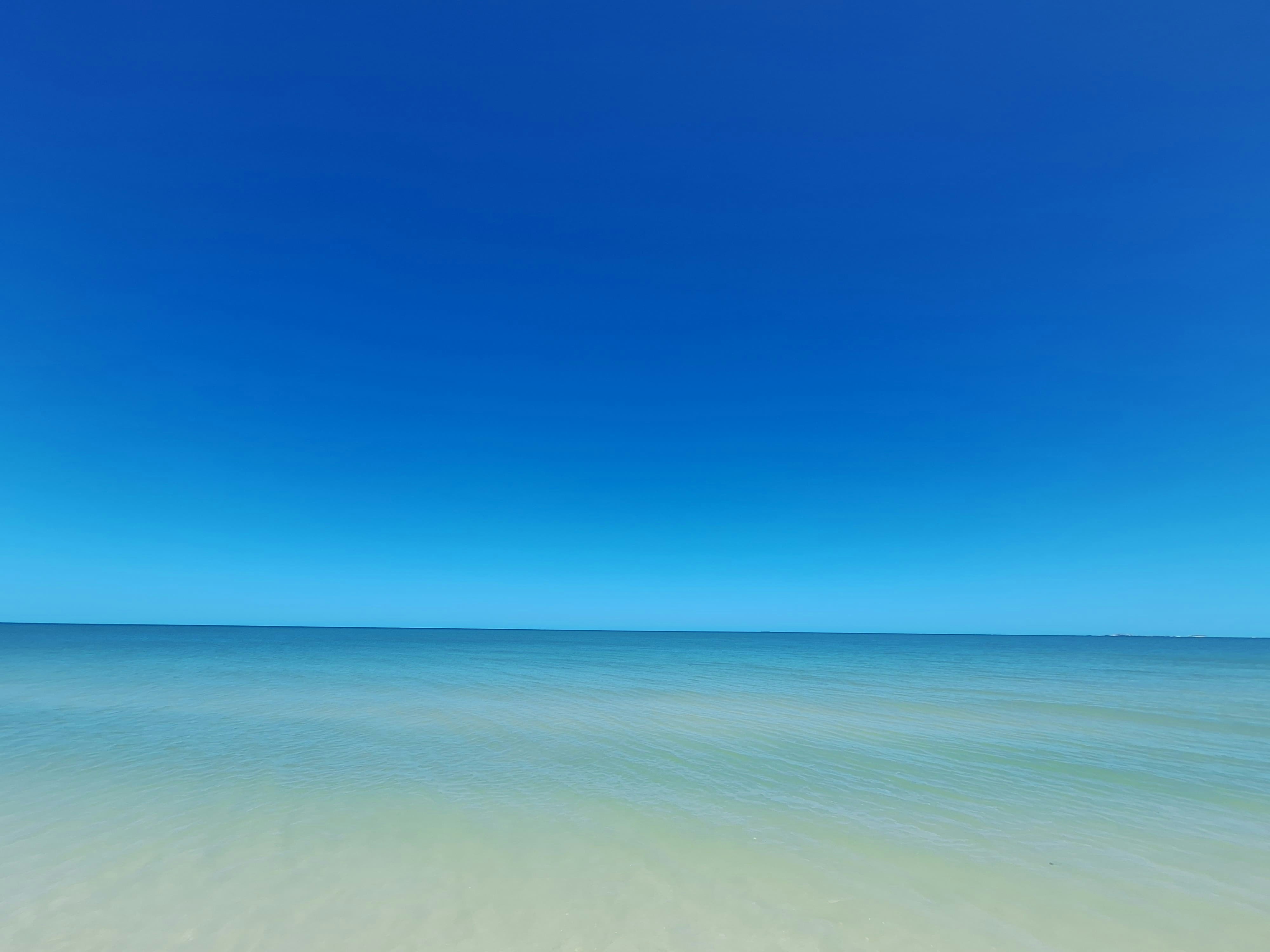 Blue sky meets calming, shallow ocean.