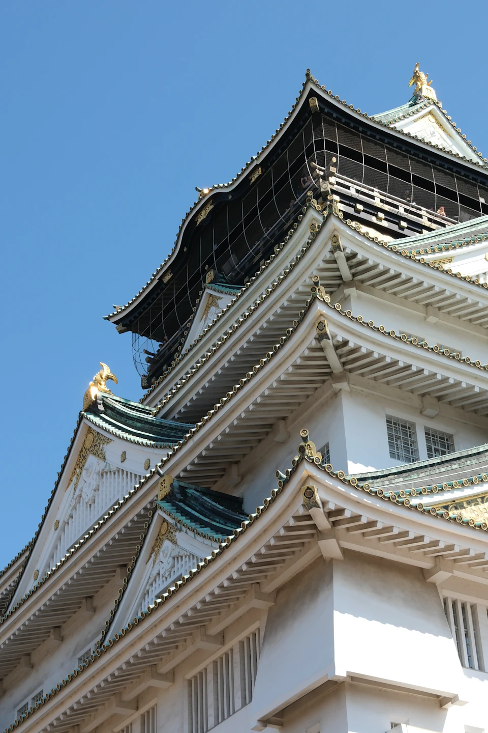 The image shows a majestic white pagoda with multiple tiers and a green roof, standing tall against a clear blue sky. The pagoda is adorned with gold accents on its corners and spires, adding to its grandeur. The perspective of the photo is from below, looking up at the pagoda, emphasizing its height and architectural beauty.

The pagoda's intricate design and vibrant colors make it an impressive sight against the backdrop of the sky.