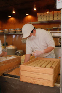 A baker arranges food in a wooden tray.